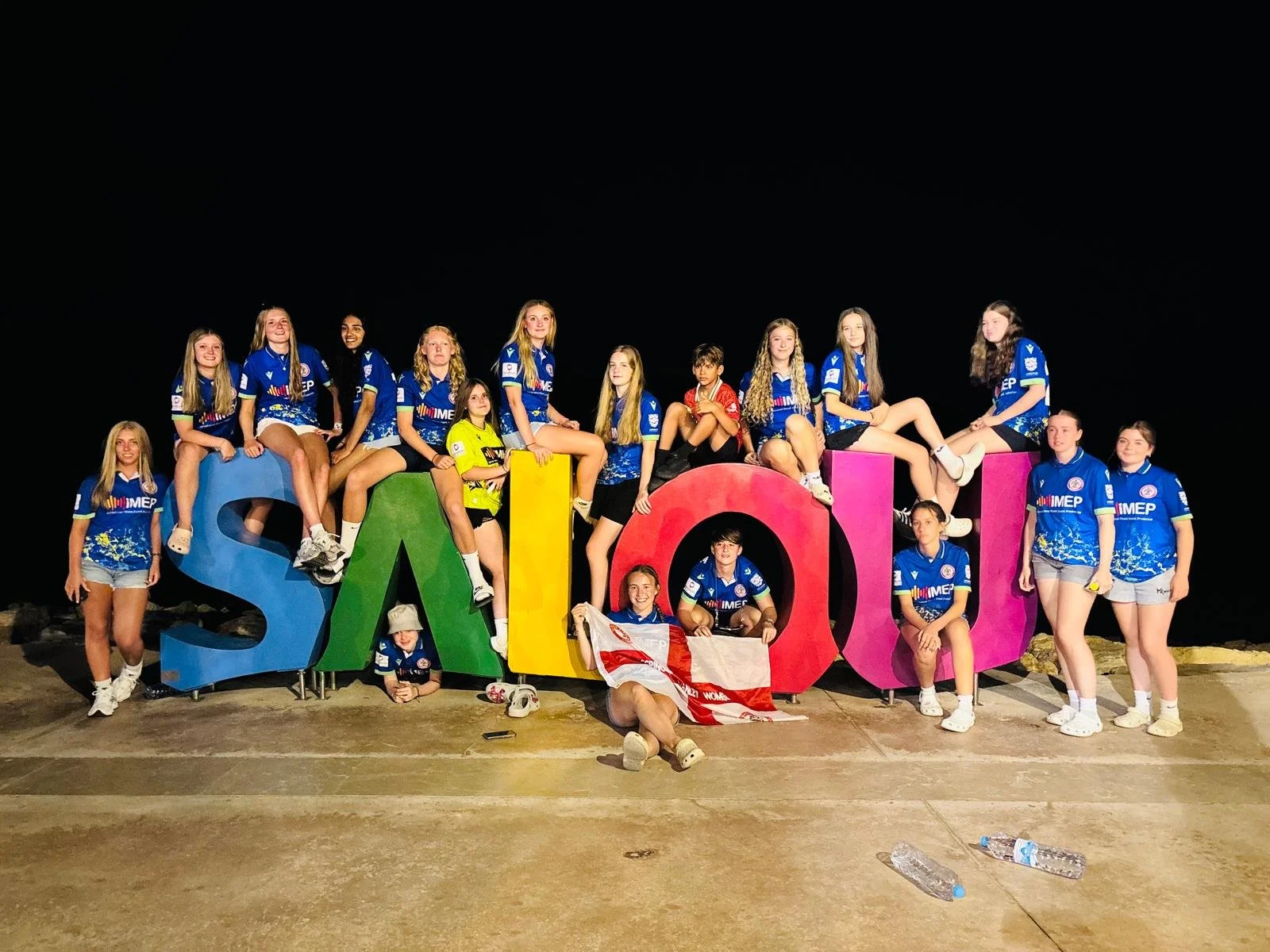 Group of young women wearing blue sports uniforms posing around colorful large letter blocks spelling "SANT