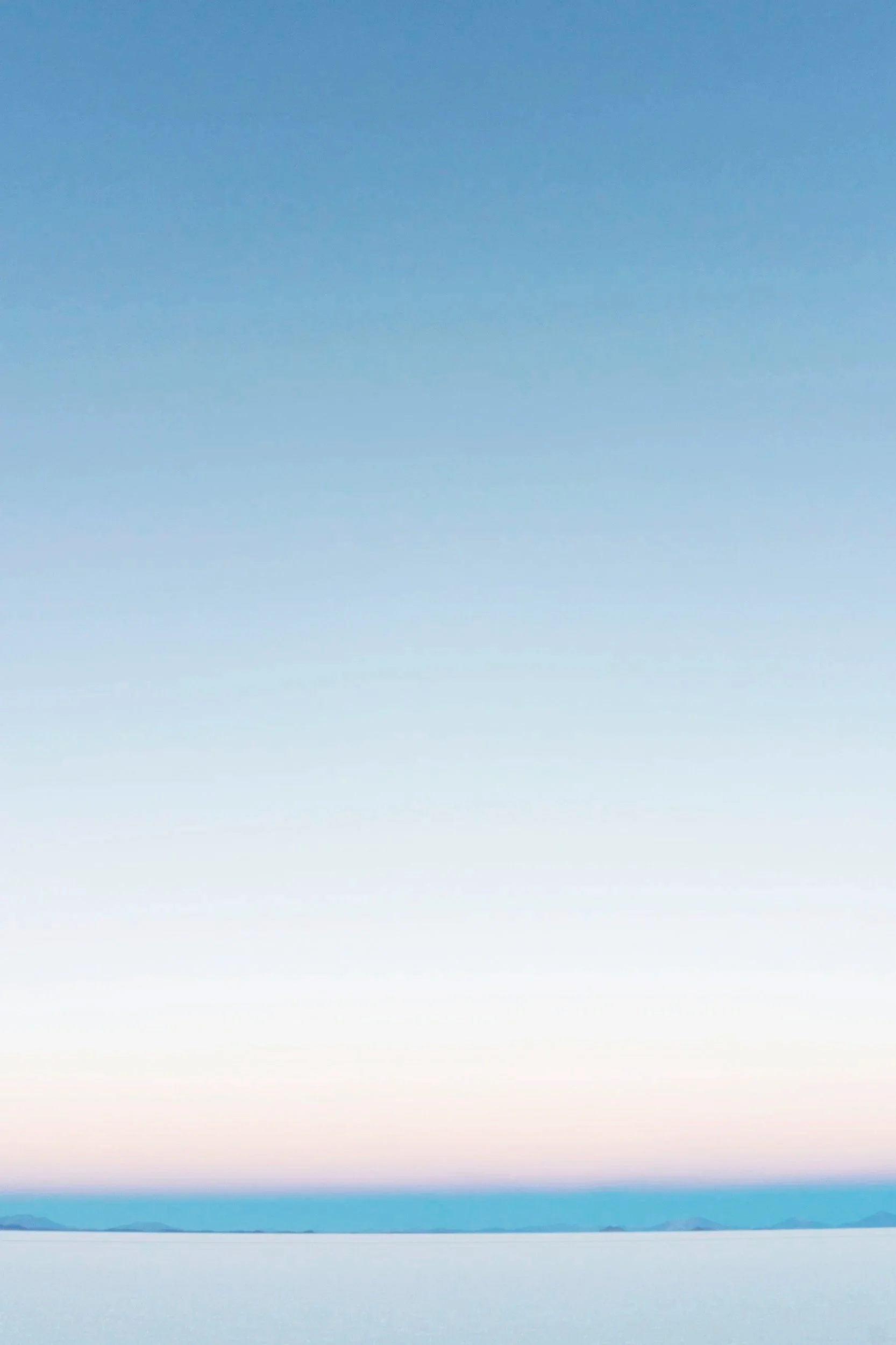 A serene landscape with a clear sky gradient from blue to pink near the horizon, a calm body of water reflecting the sky, and distant mountains or islands on the horizon.