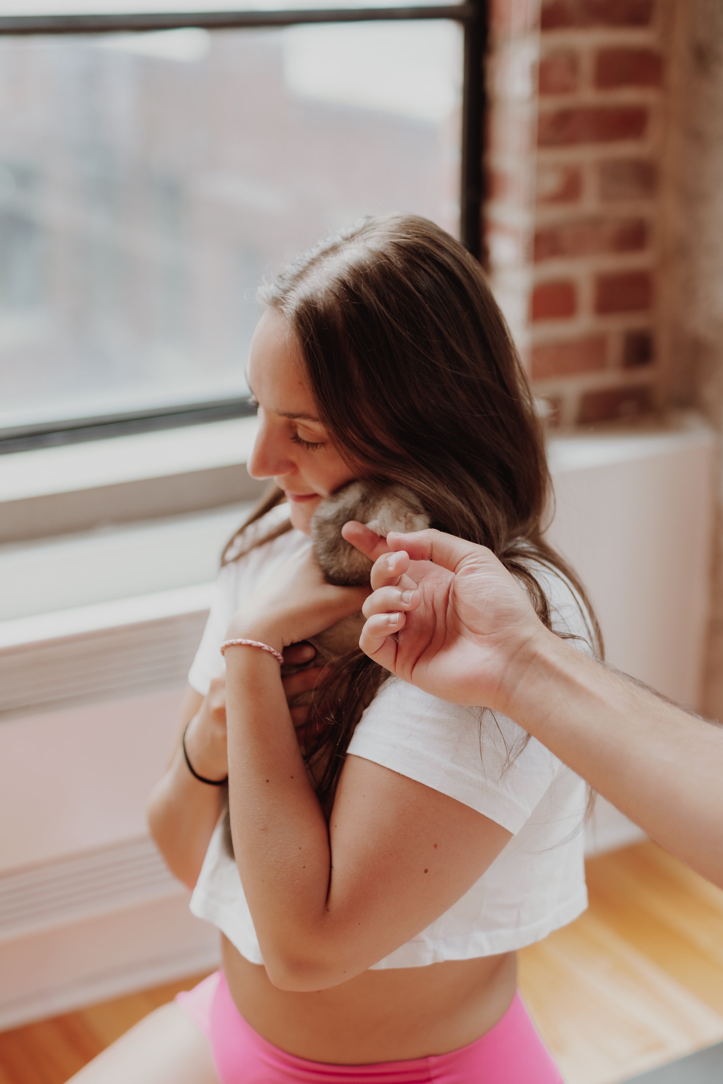 A woman with long brown hair holding a kitten close to her face indoors near a window.