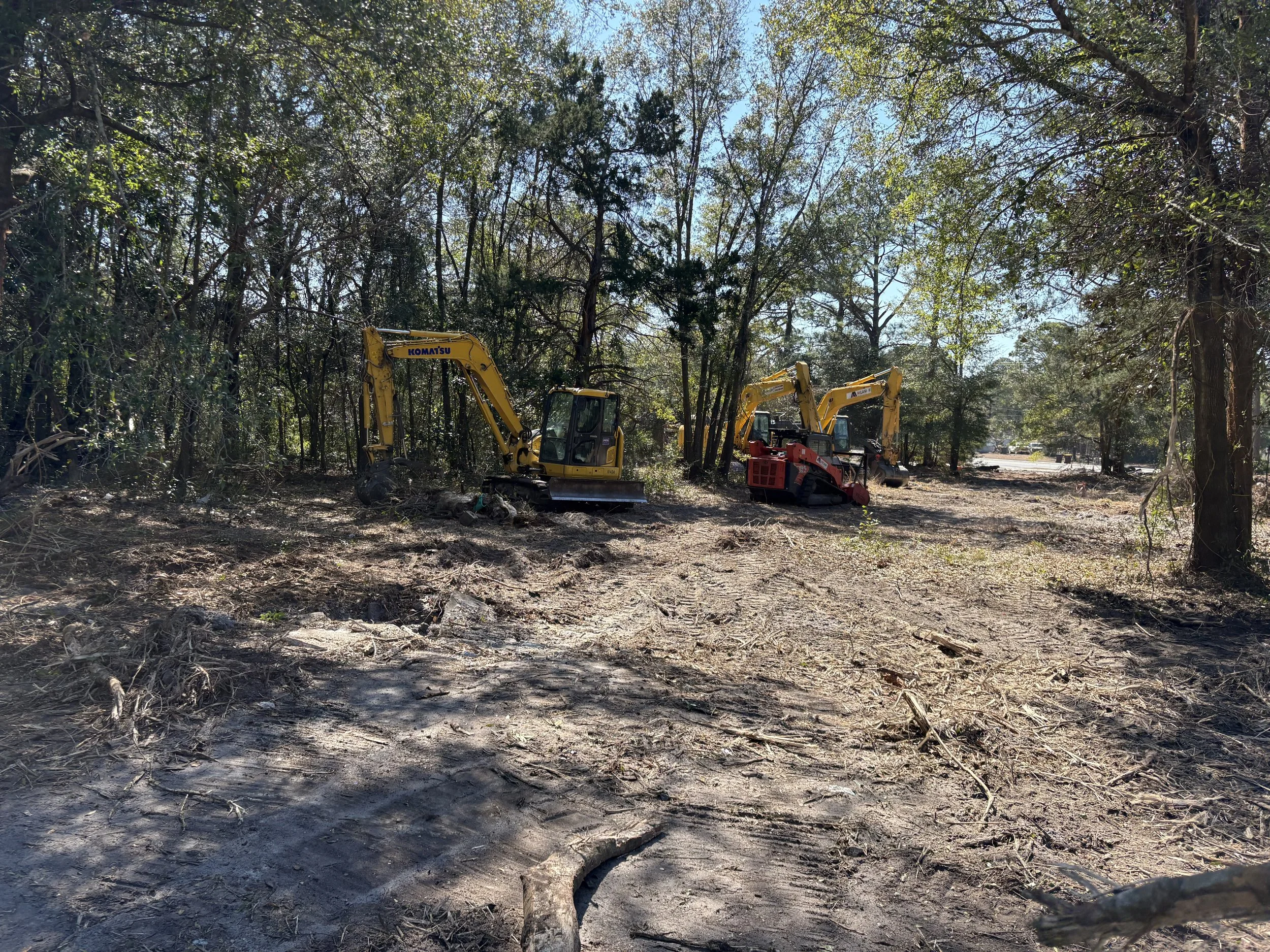 Two yellow and red excavators working on clear cut forested area under a partly cloudy sky.