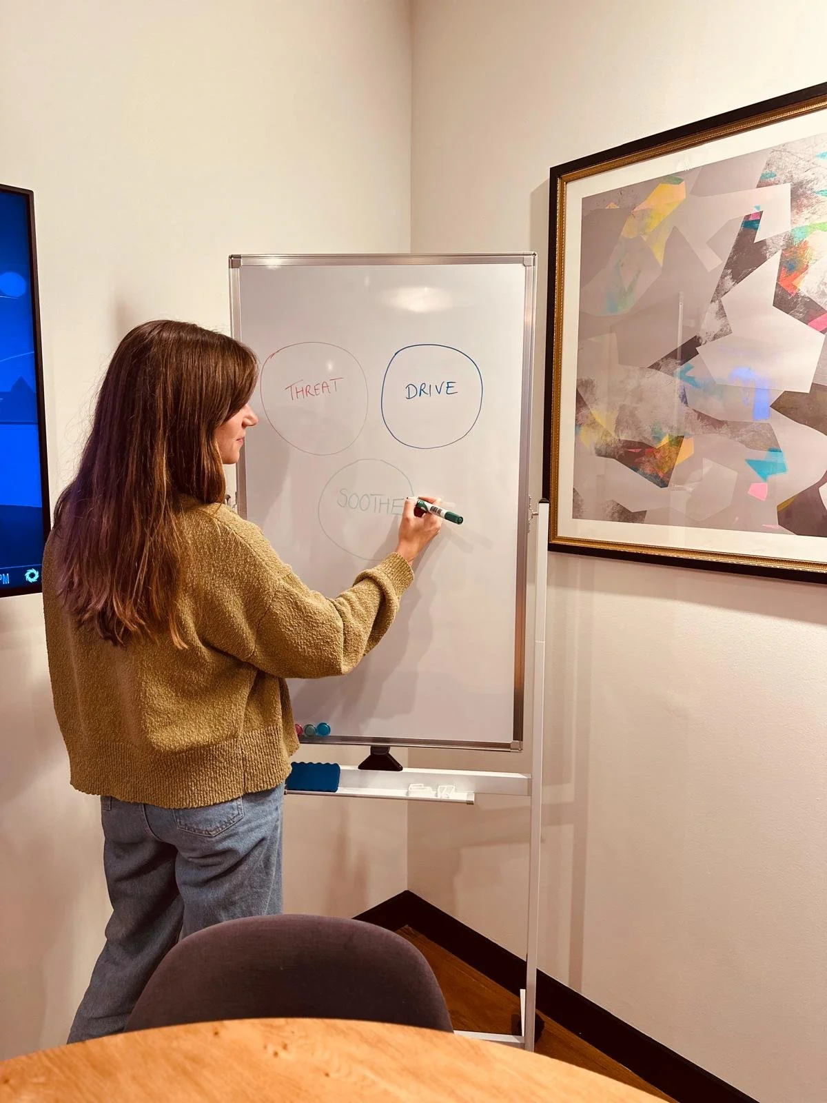 Therapist standing at a whiteboard during a workshop, drawing three circles labelled 'Threat', 'Drive', and 'Soothe' as part of a psychological model.