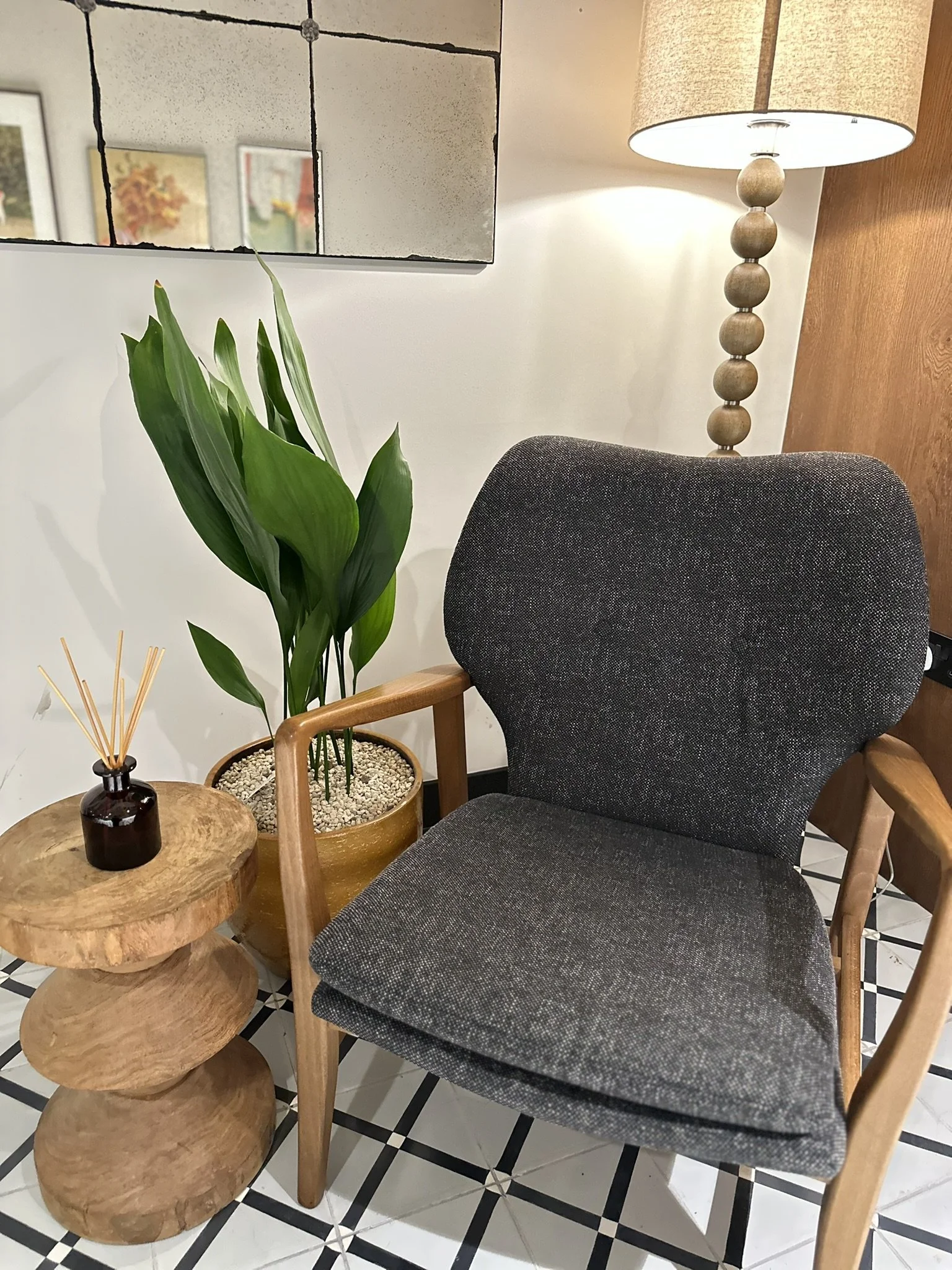 Grey chair beside a wooden table holding a reed diffuser and a small potted plant, creating a calm, minimalist setting.