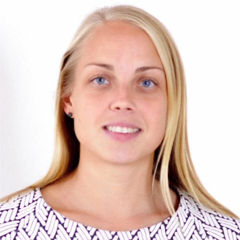 Ung kvinna med blont hår, blå ögon och ljus hud, leende, mot en vit bakgrund, bär en svart och vit mönstrad topp.