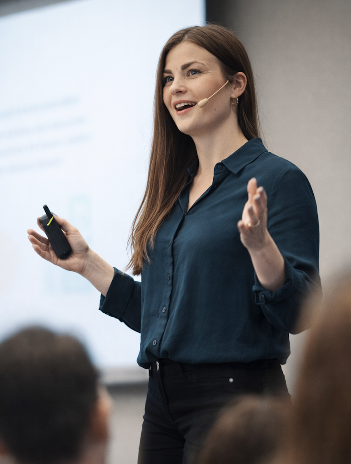 Kvinna som håller i en fjärrkontroll och talar inför en publik i ett konferenserum.