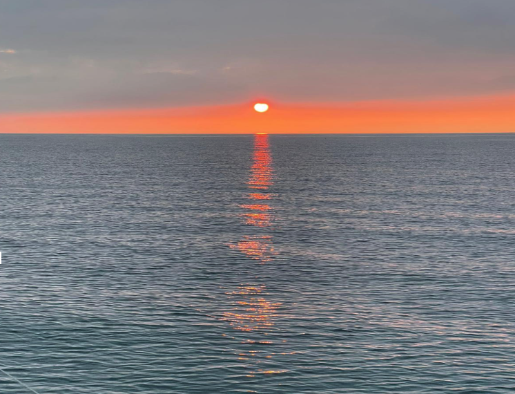 Sunset over the ocean with the sun just above the horizon and its reflection on the water.