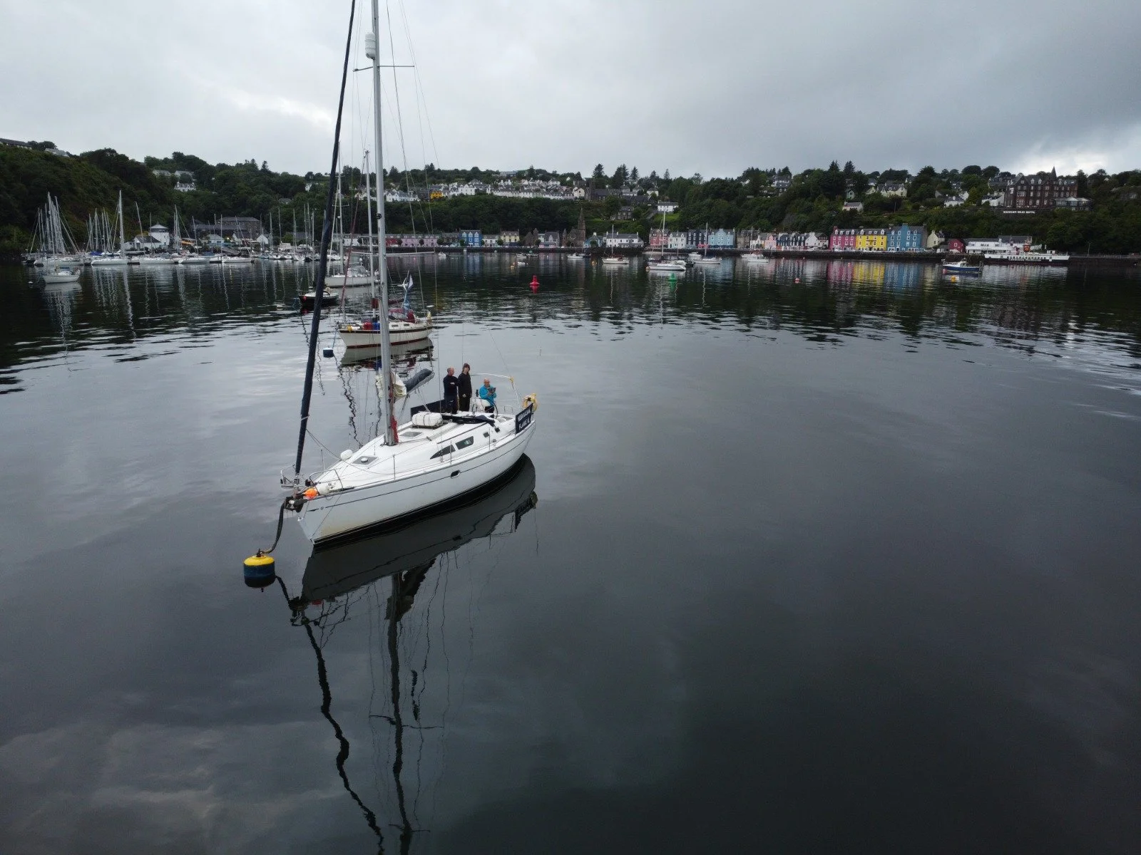 A marina with a sailboat and a town with colorful buildings in the background under an overcast sky.