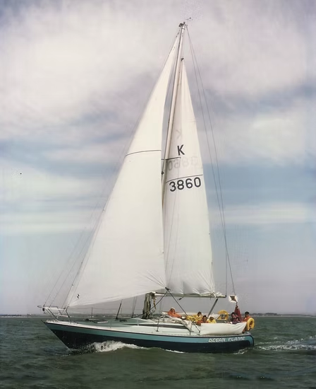 A sailboat with white sails on water under a cloudy sky.