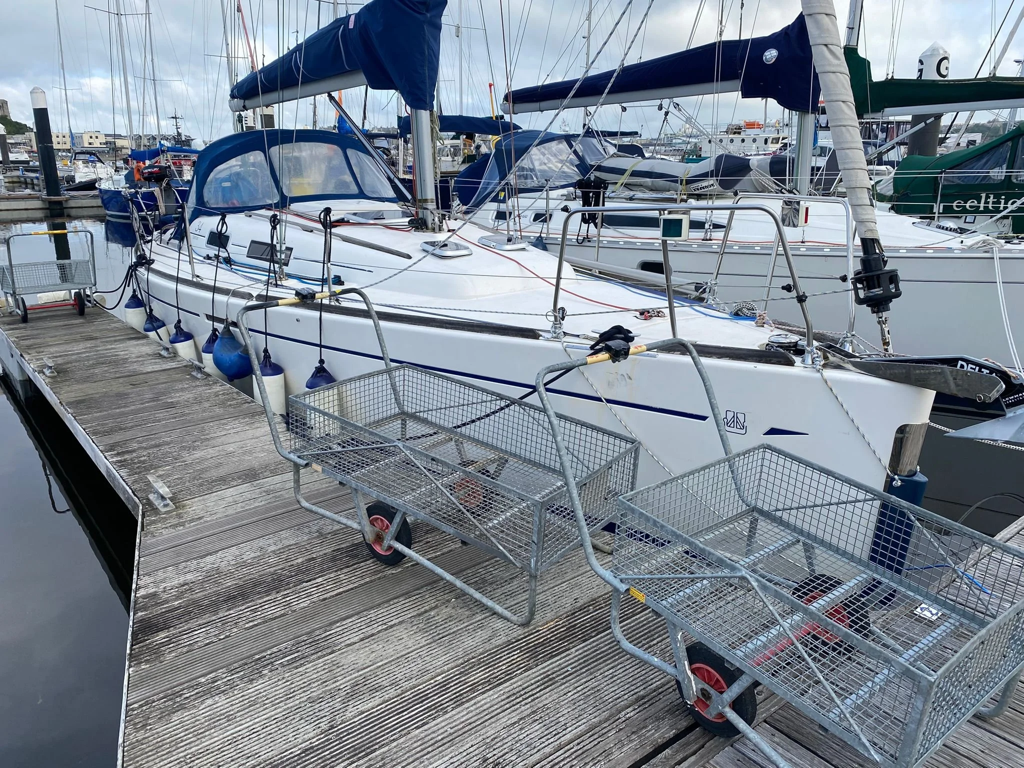 A white sailboat docked at a marina with metal carts on the wooden dock in the foreground.