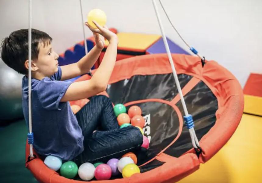 Young boy playing in a ball pit with colorful plastic balls, holding a yellow ball in his hand.