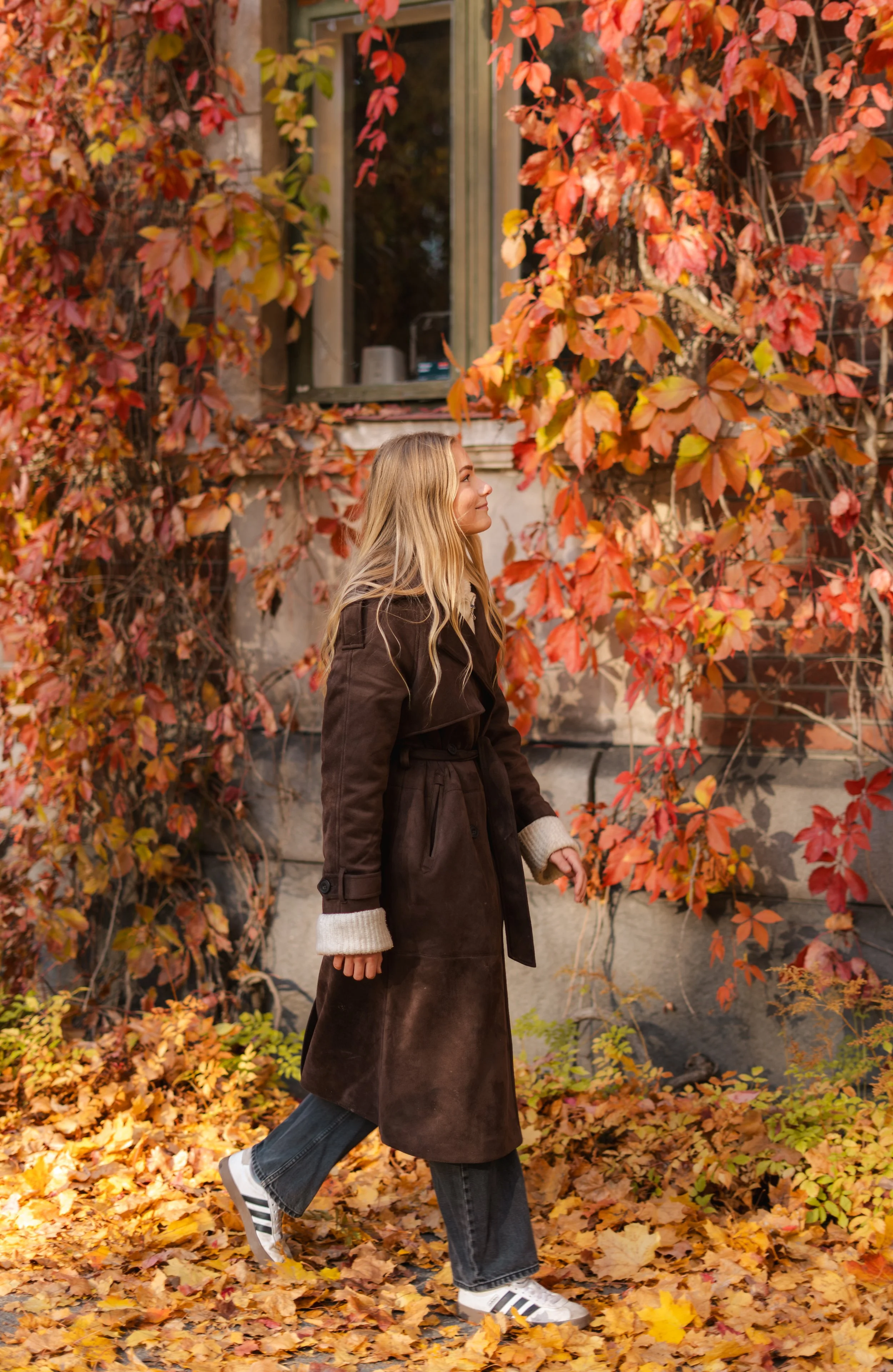 Nuori nainen kävelee syksyisessä puistossa, ympärillään punaiset ja keltaiset lehtipuut ja lehtikatto.