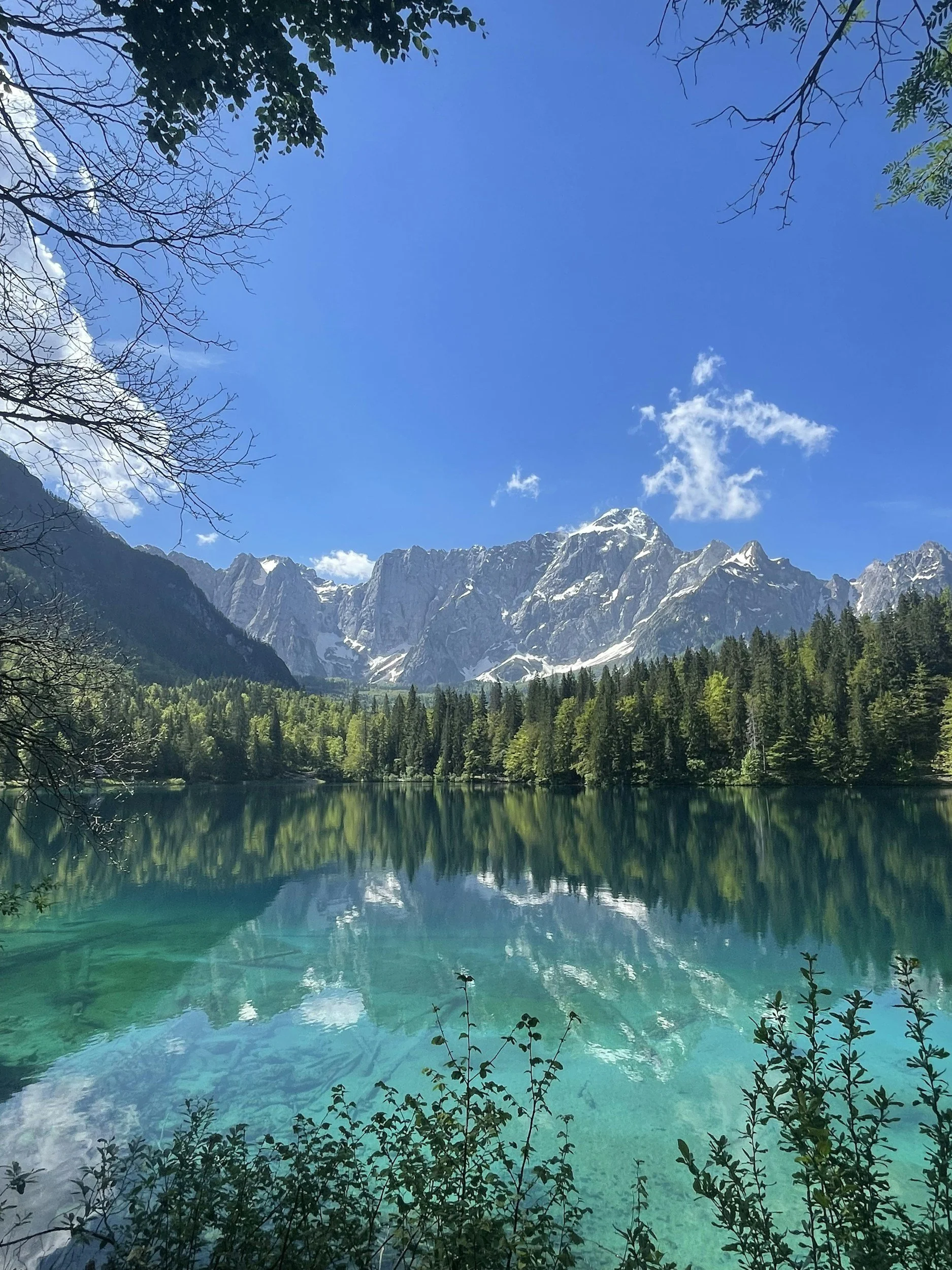 A wide-angle shot of a smooth, glass-like mountain lake perfectly reflecting the surrounding snow-capped peaks and clear blue sky. The surface is completely undisturbed, with crisp, sharp reflections.
