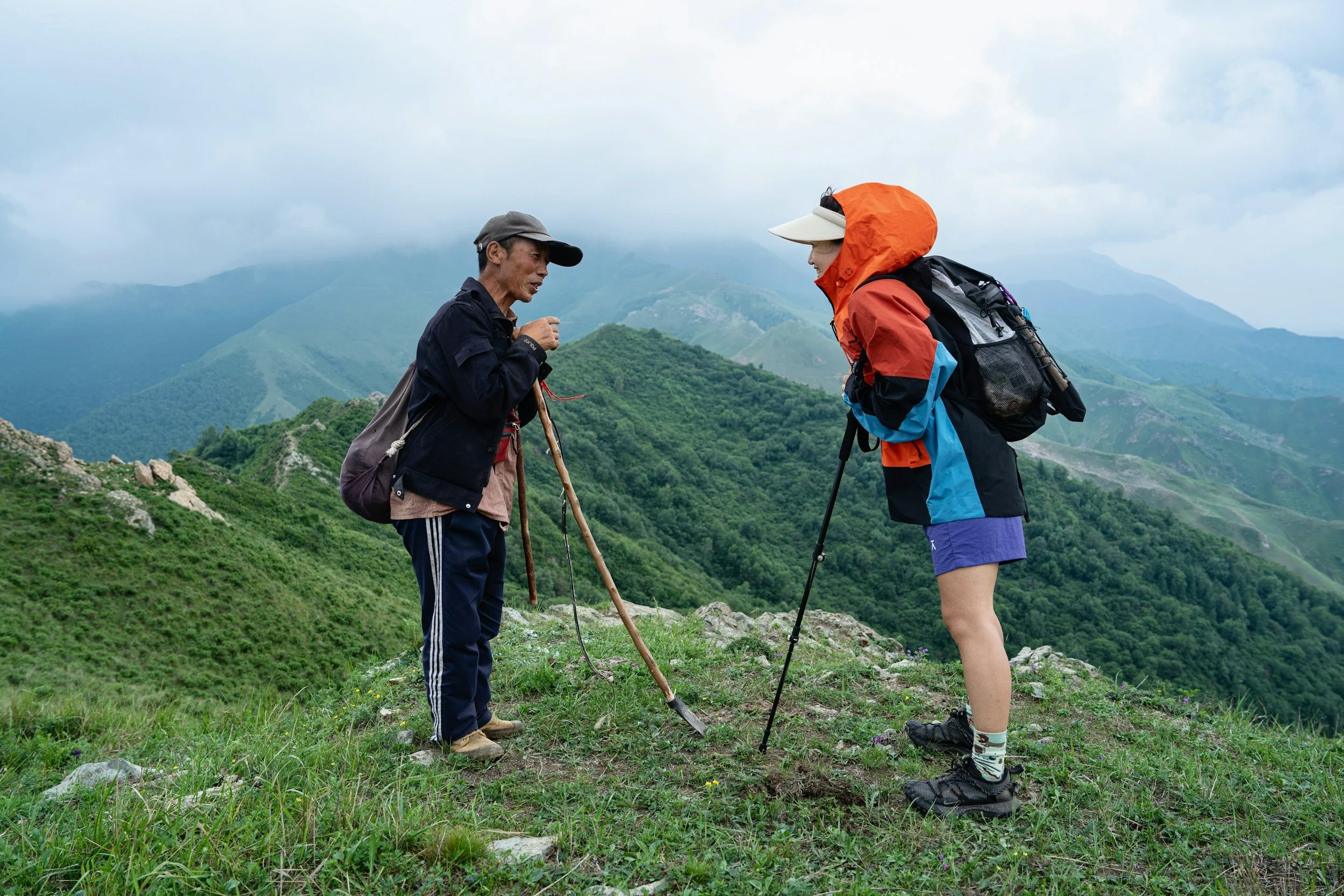 Two hiking partners leaning on walking sticks after summiting a mountain together