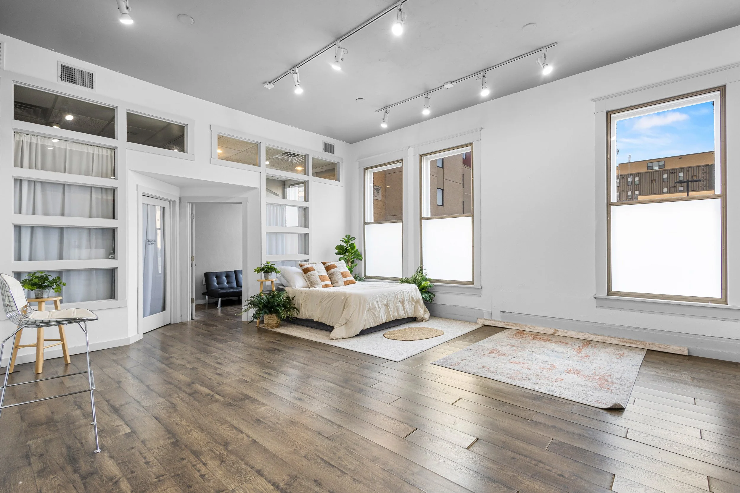 Spacious, modern studio apartment with a bed, hardwood floors, large windows, and minimal decor.