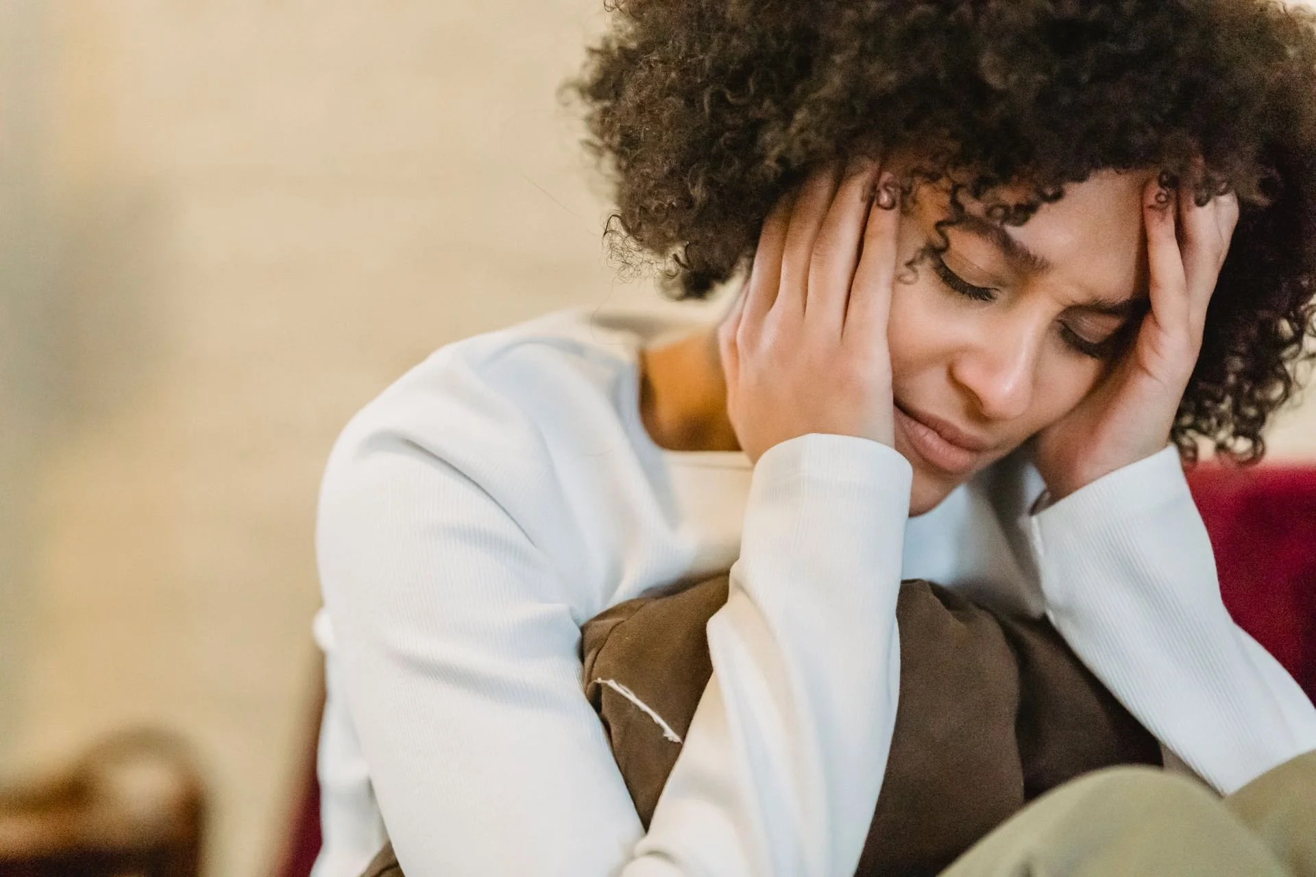 A stressed professional holding her head, illustrating systemic depletion and physiological strain addressed by the WellThera PHIQ framework.