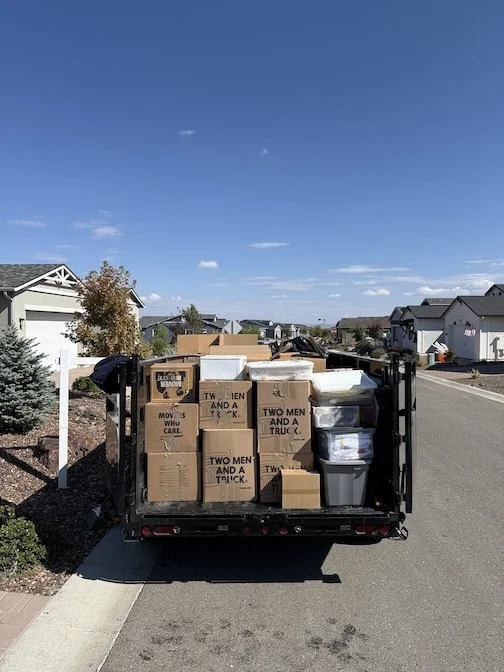 A trailer loaded with cardboard boxes and plastic containers parked on a residential street.