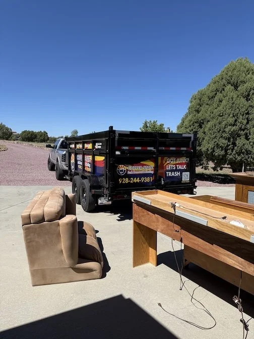 A black utility truck parked on a concrete driveway with a beige couch and a wooden table nearby, under a bright blue sky.