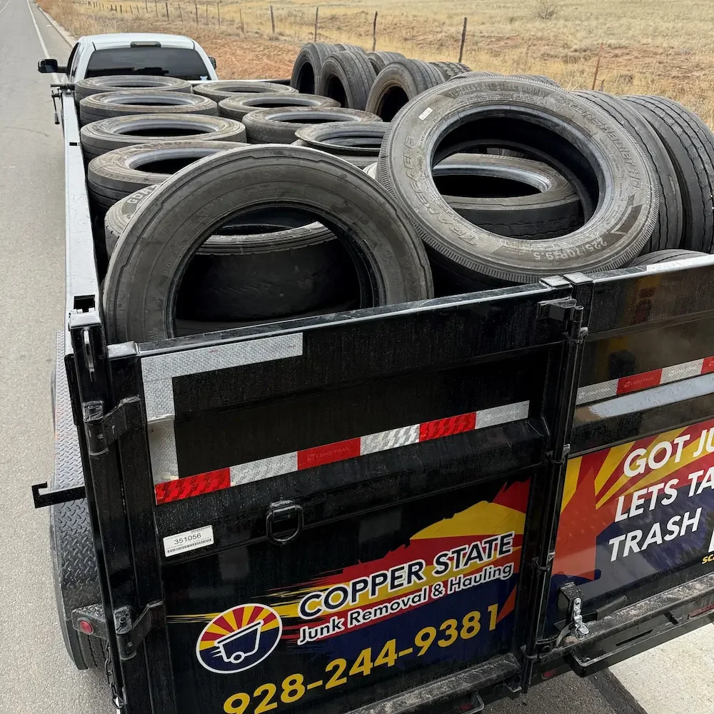 A Copper State Junk Removal & Hauling truck filled with old tires being driven away