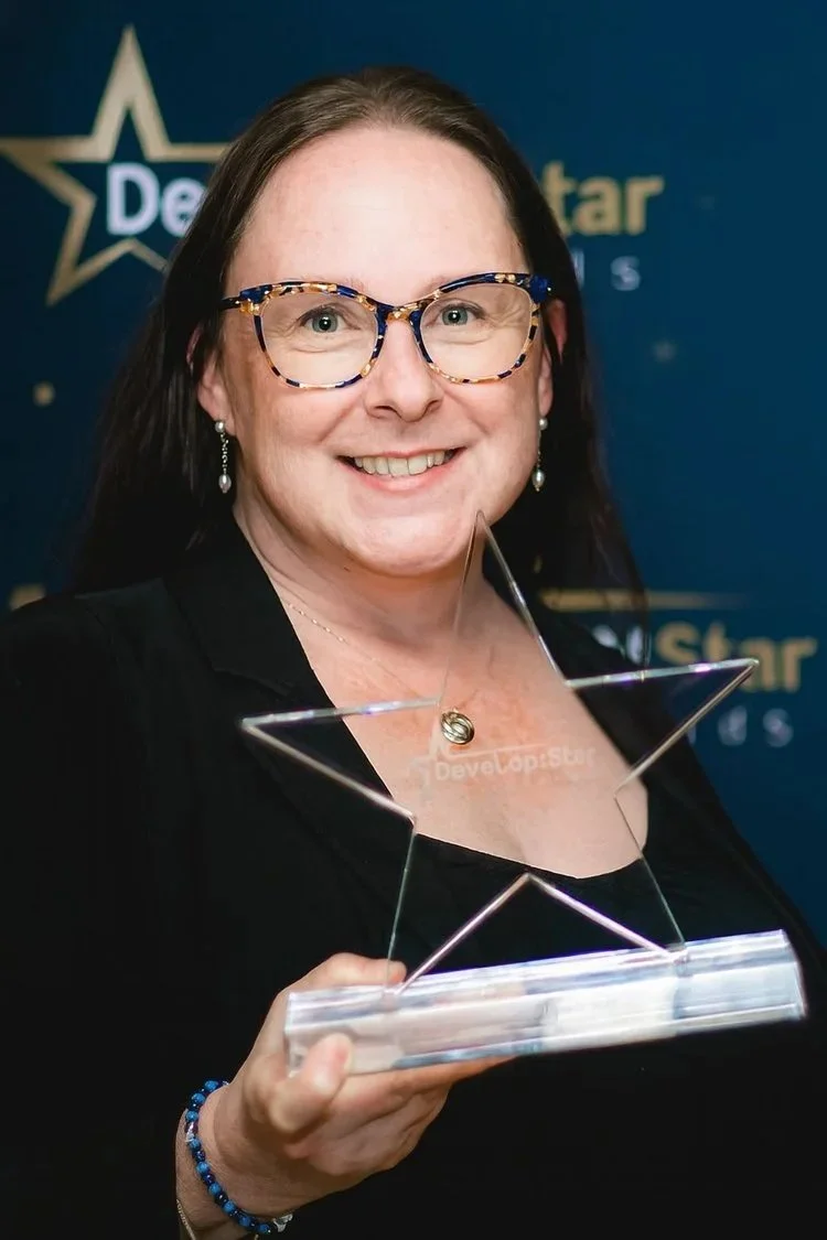 A woman with glasses and earrings holding a star-shaped award trophy in front of a blue background with the logos of DevelopStar.