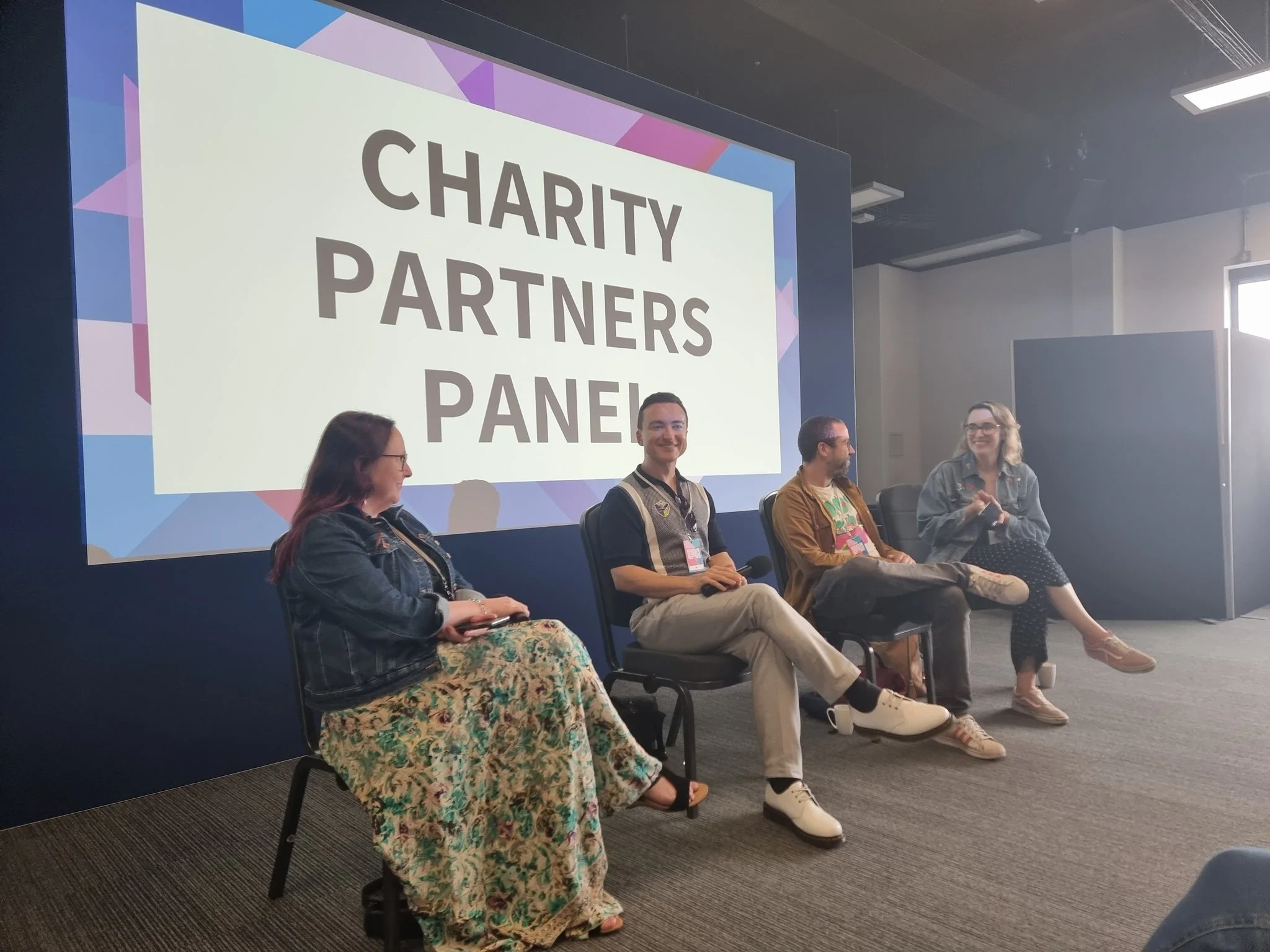 A panel discussion at a charity event with five people seated in front of a large screen that reads 'Charity Partners Panel.'