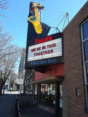 The sign of a Roy Rogers restaurant with a neon cowboy boot on top and a message board reading 'WE'RE IN THIS TOGETHER.'
