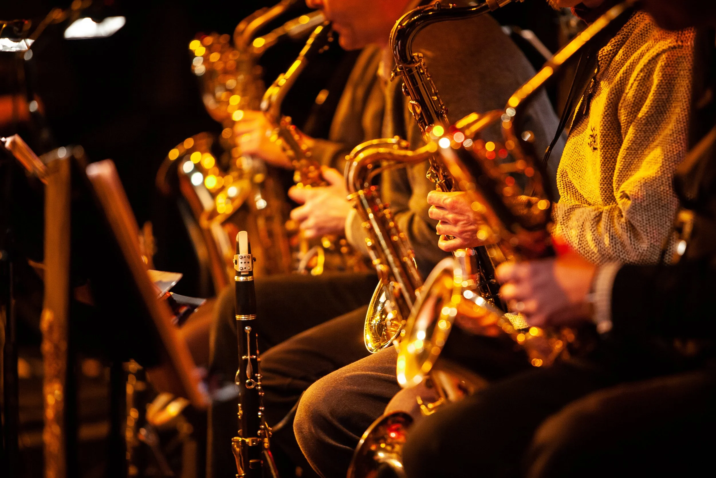 A row of musicians playing saxophones in a dimly lit setting, with a focus on their hands and instruments.