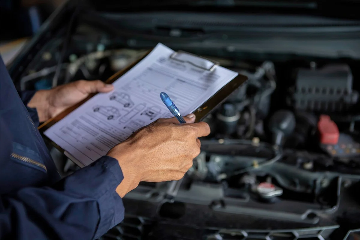 Auto mechanic inspecting under the hood of a vehicle using clipboard with document to record the vehicles condition.