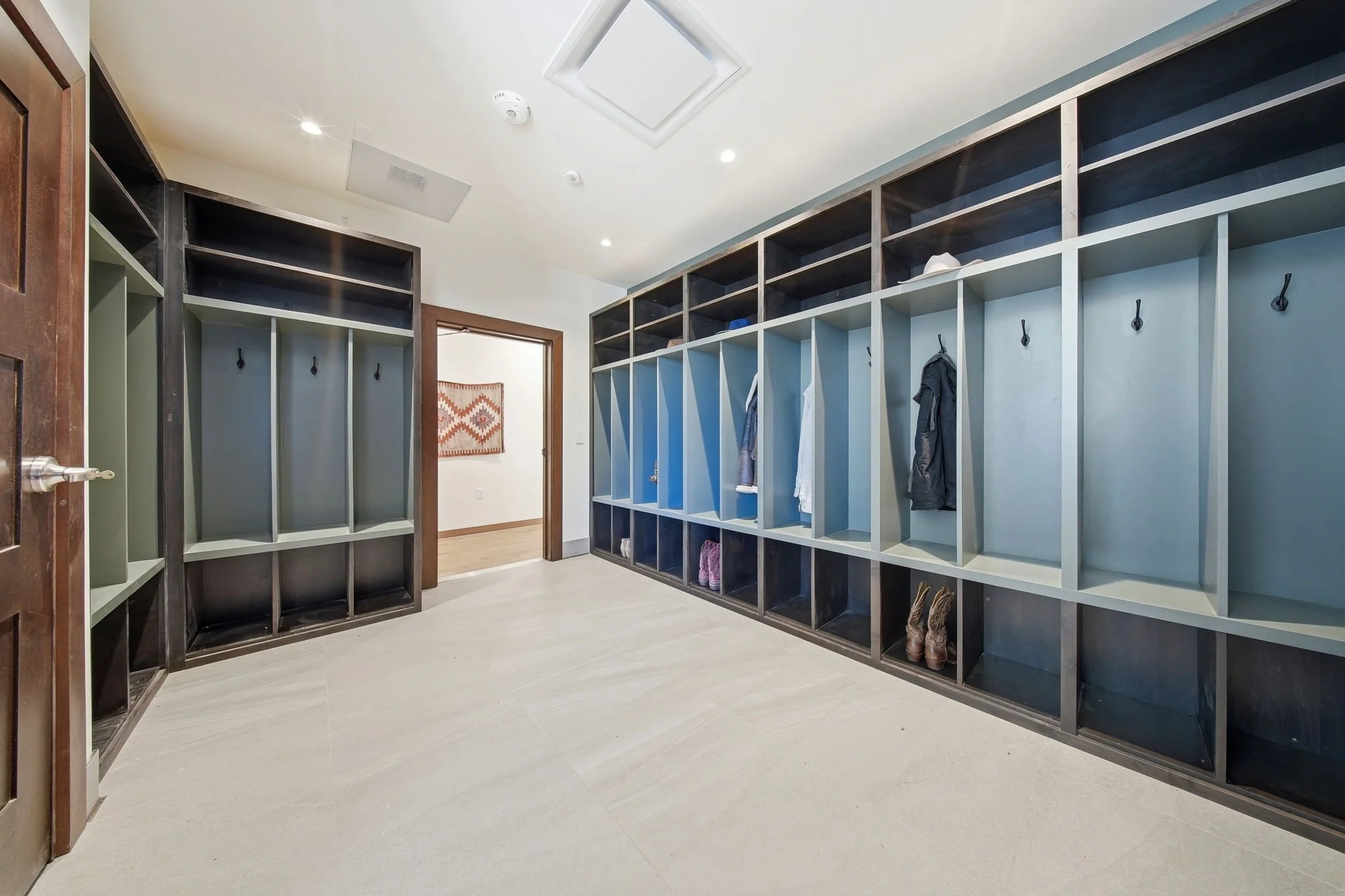 Empty mudroom with organized cubbies and hooks, some shoes and boots stored, ceiling with lights and ventilation