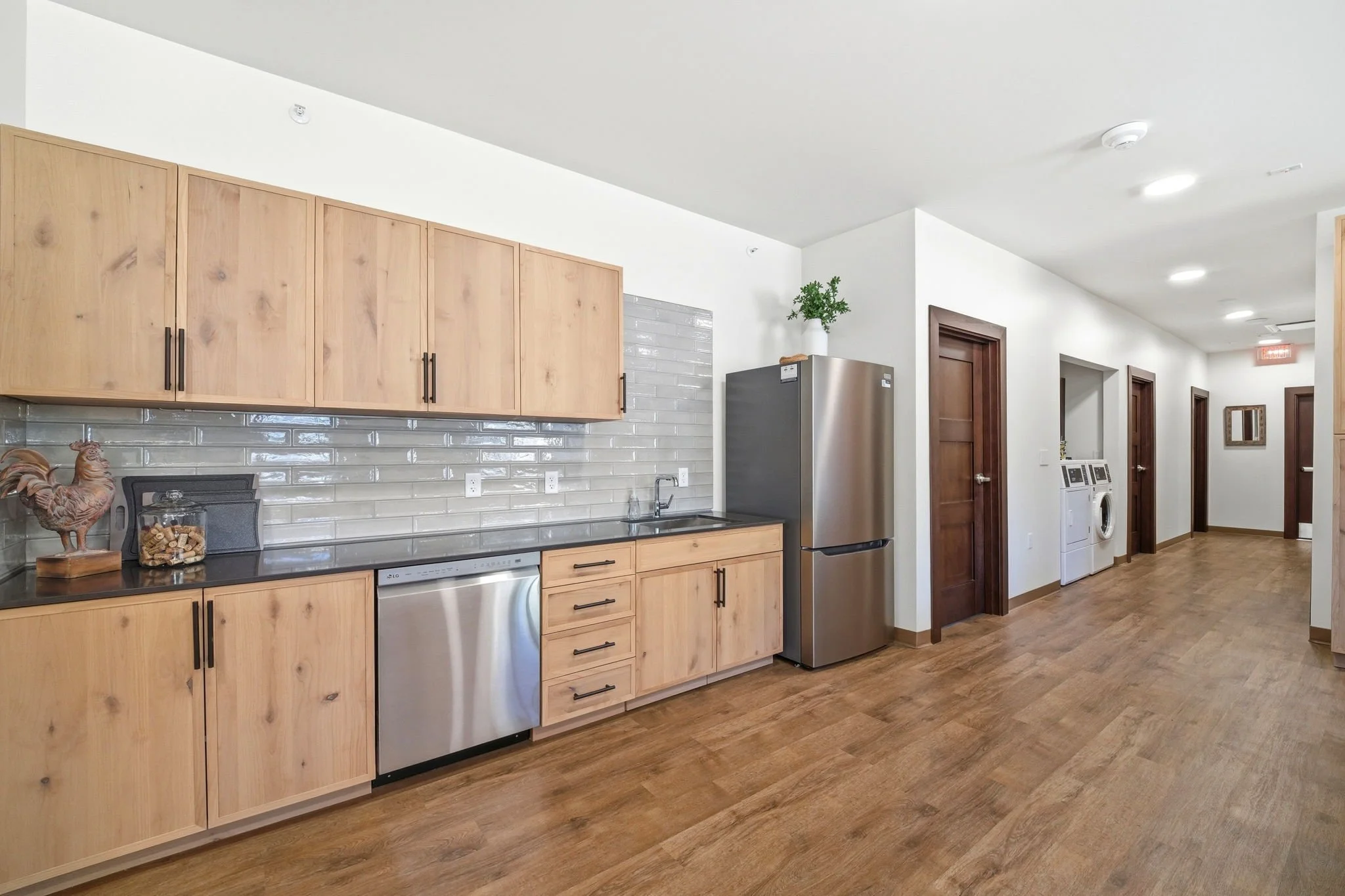 Kitchen area with wooden cabinets, stainless steel refrigerator, washing machine, and wooden flooring.