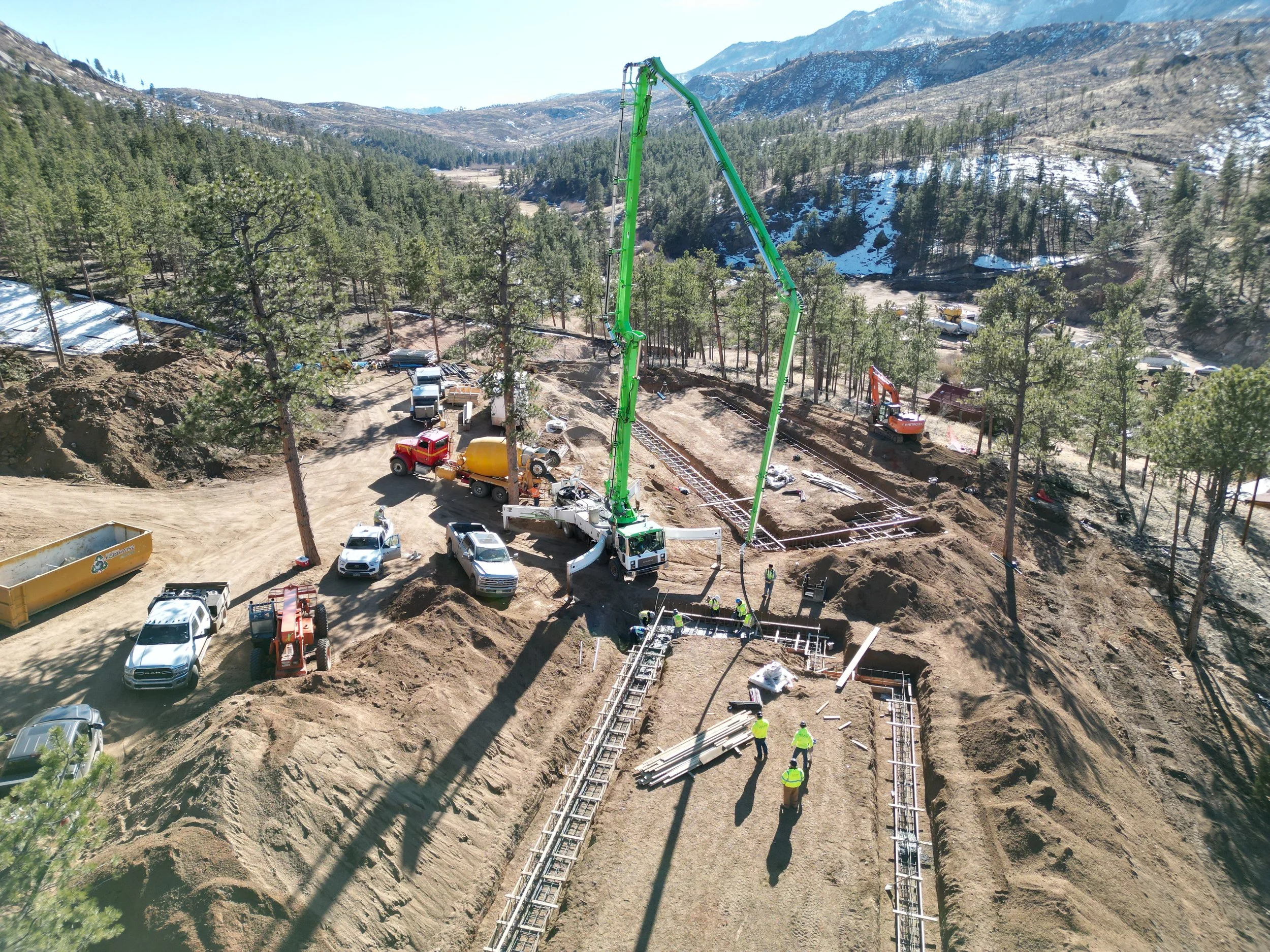 Construction site with workers and heavy machinery building a road through a forested mountainous area.