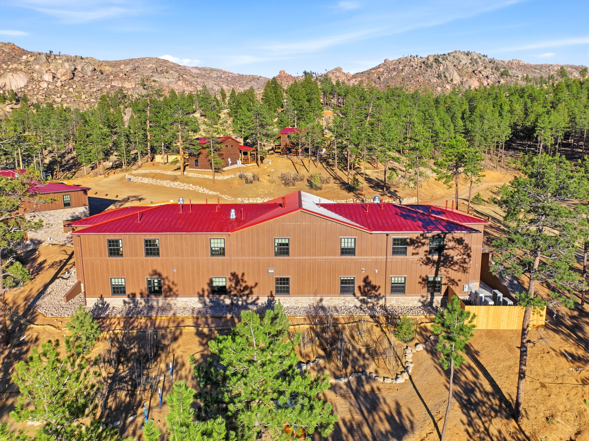 A residential area with brown buildings and red roofs surrounded by trees and mountainous terrain in the background.