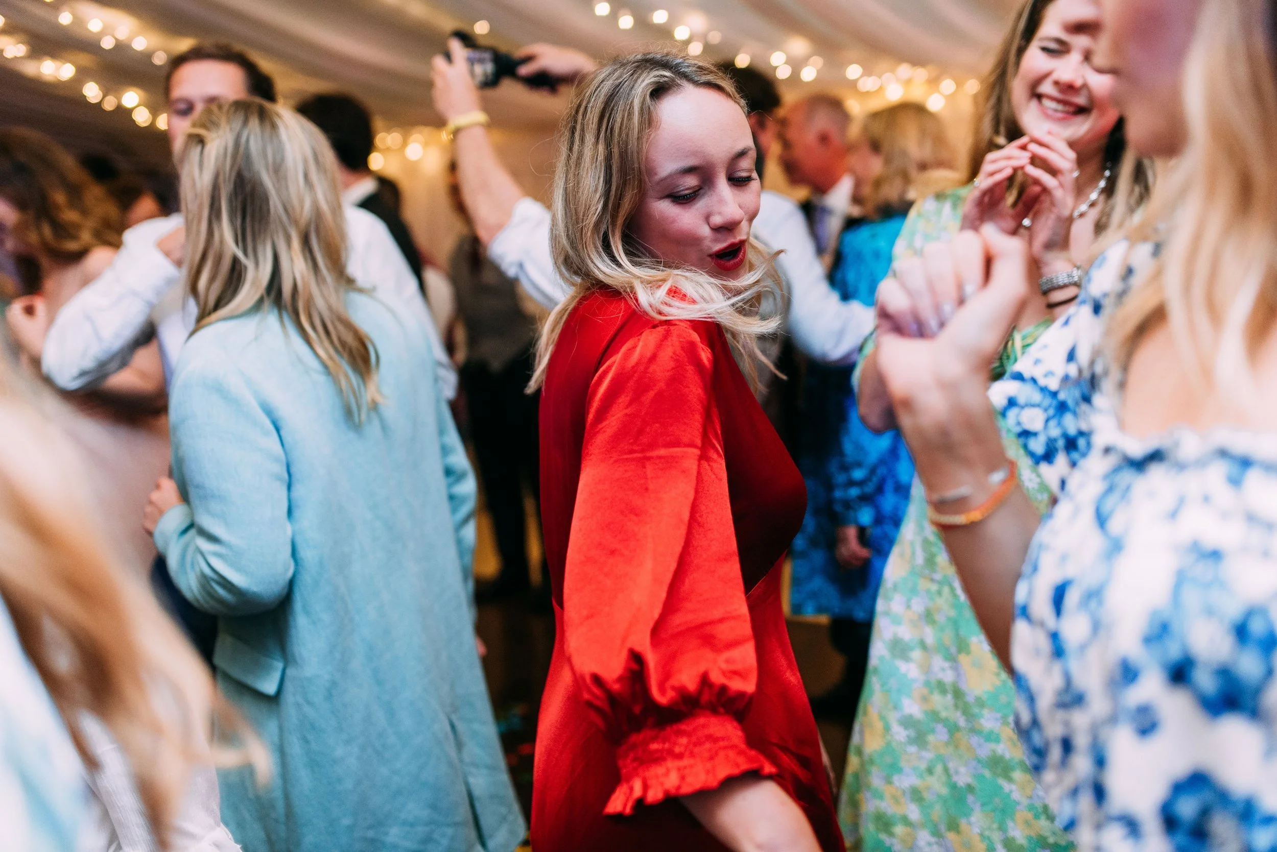 People dancing and enjoying themselves at a lively indoor event or party, with string lights hanging from the ceiling.
