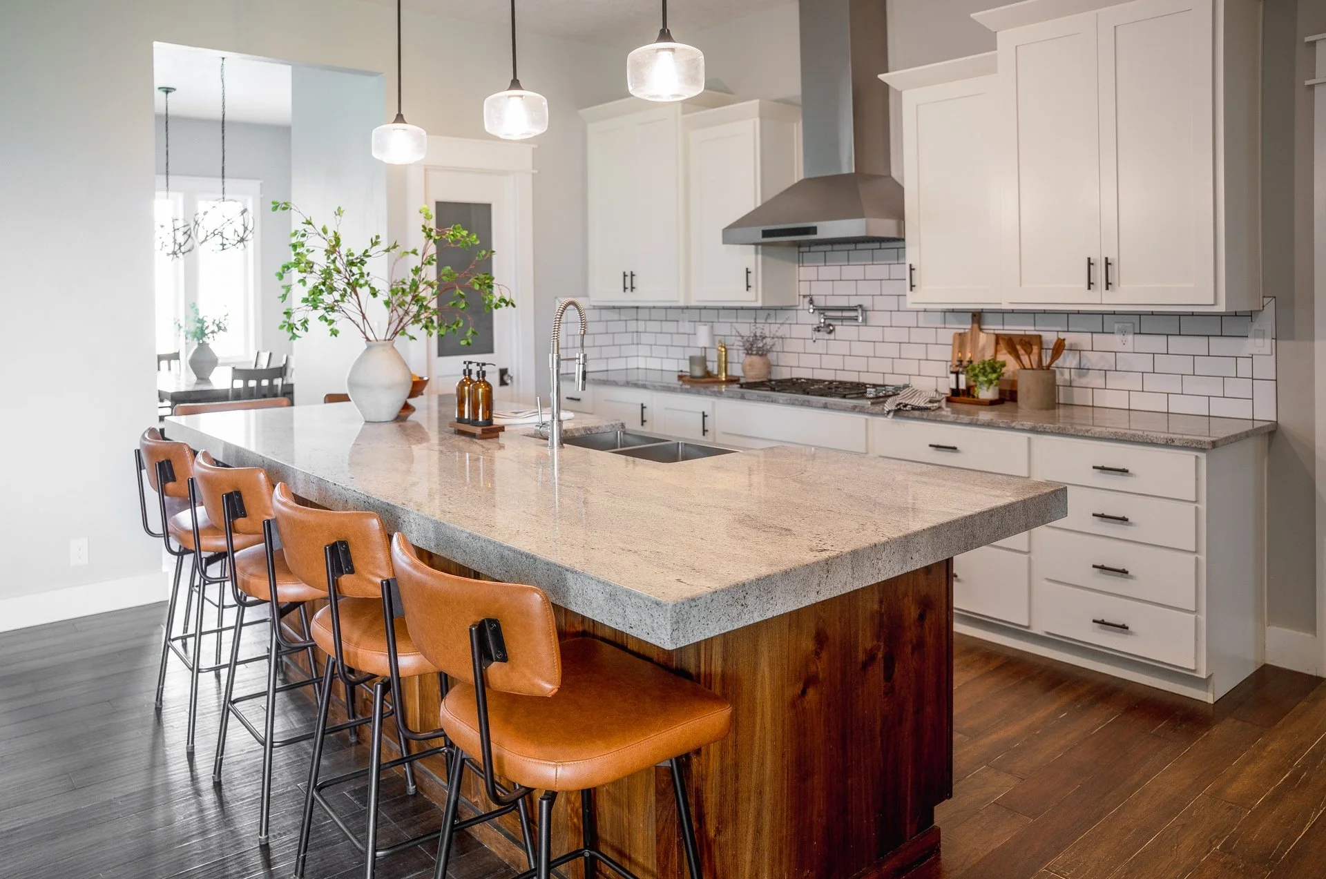Modern kitchen with white cabinets, a large island with tan leather chairs, and pendant lighting, perfect for sharing family meals together.