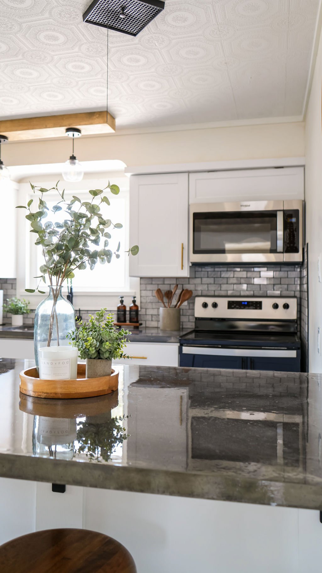 Modern kitchen with white cabinets, gray backsplash, black countertop, and stainless steel microwave oven. Decor includes vases with greenery on a marble counter.