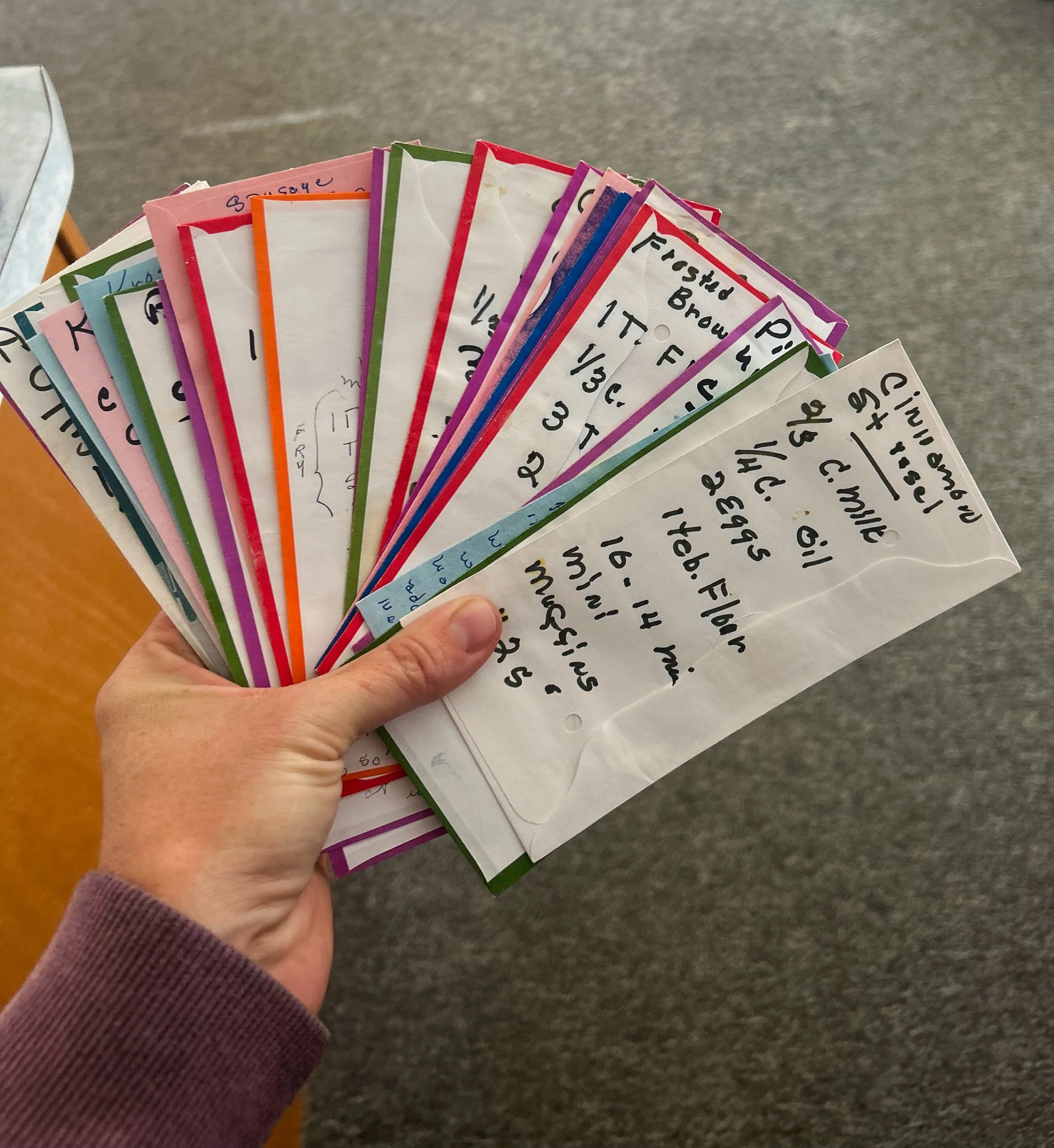 Hand holding a fan of Sunday offering envelopes with handwritten recipes.