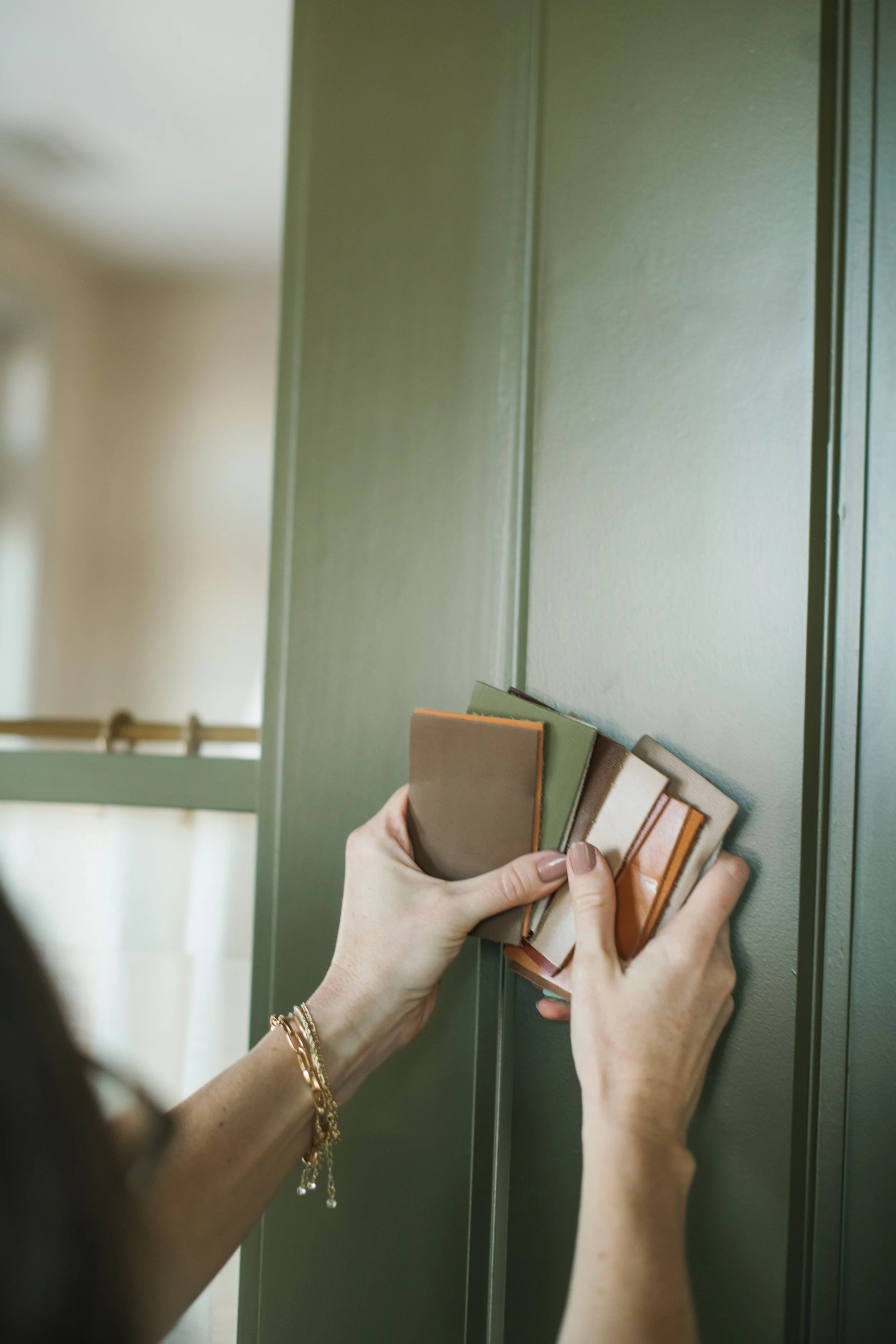Interior Designer, Trista Cross, holding a set of small paint color samples in her hand against a green wall.