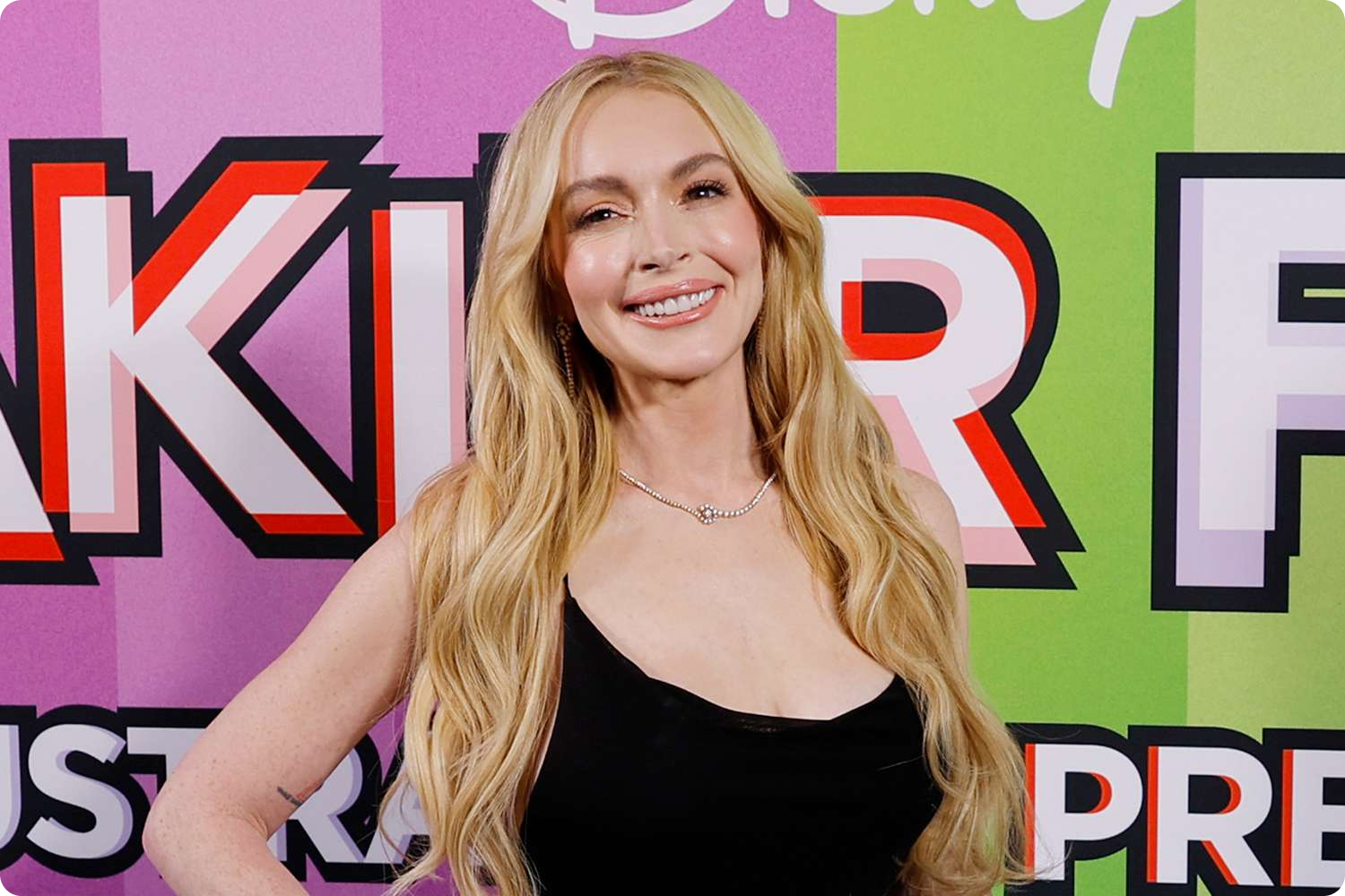 A woman with long, wavy red hair and blue eyes sitting indoors with a neutral expression.
