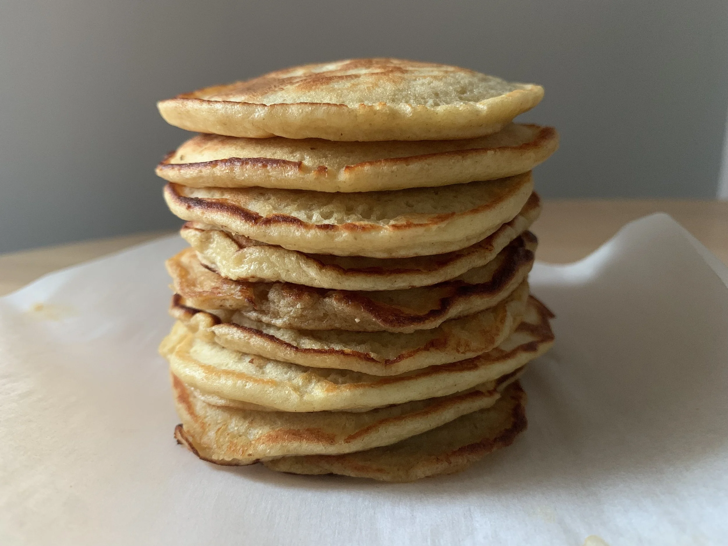 Stack of ten golden brown pancakes on white paper.