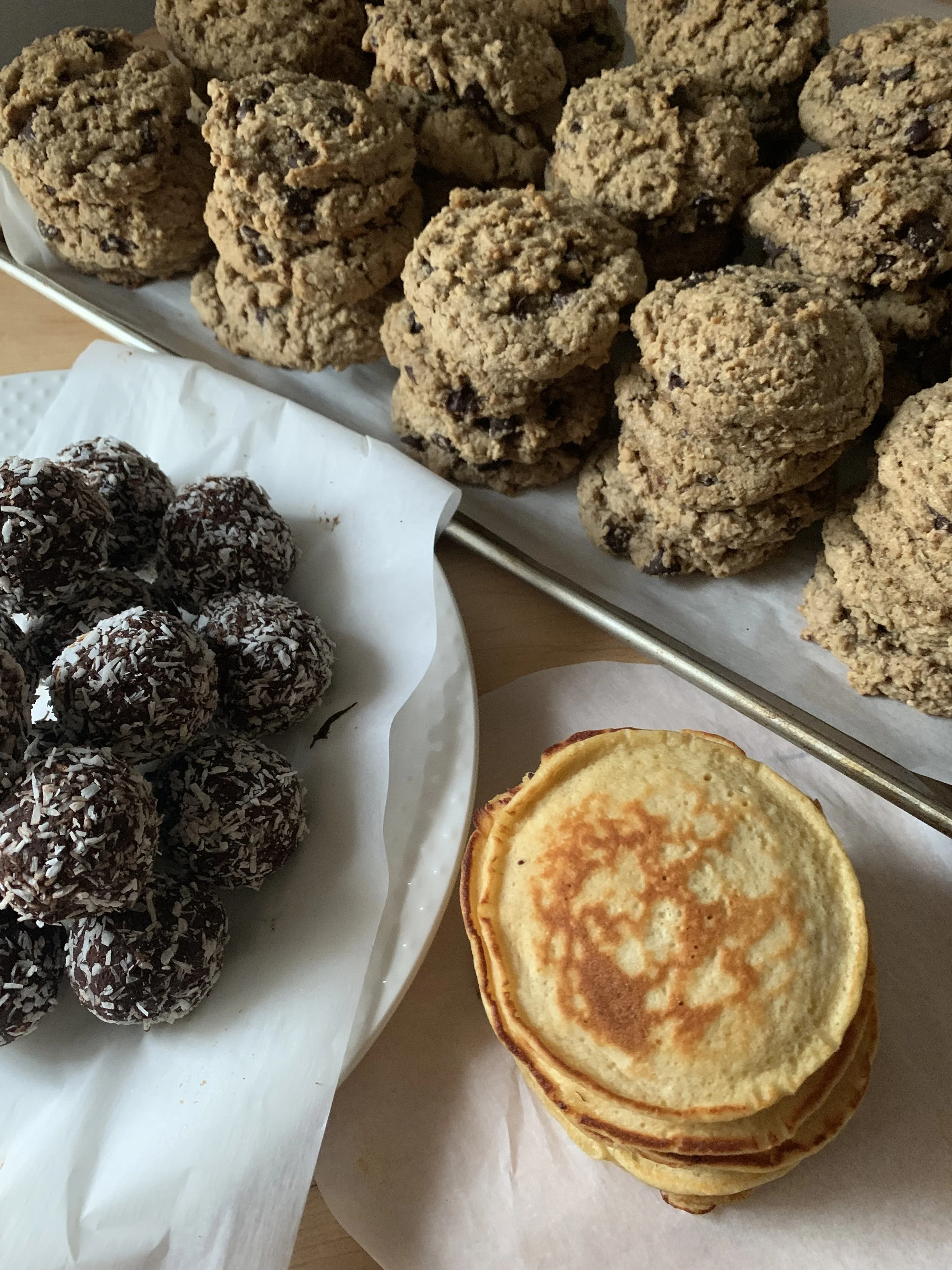 Assorted homemade cookies including oatmeal chocolate chip cookies, chocolate coconut balls, and mini pancakes stacked in a pyramid.