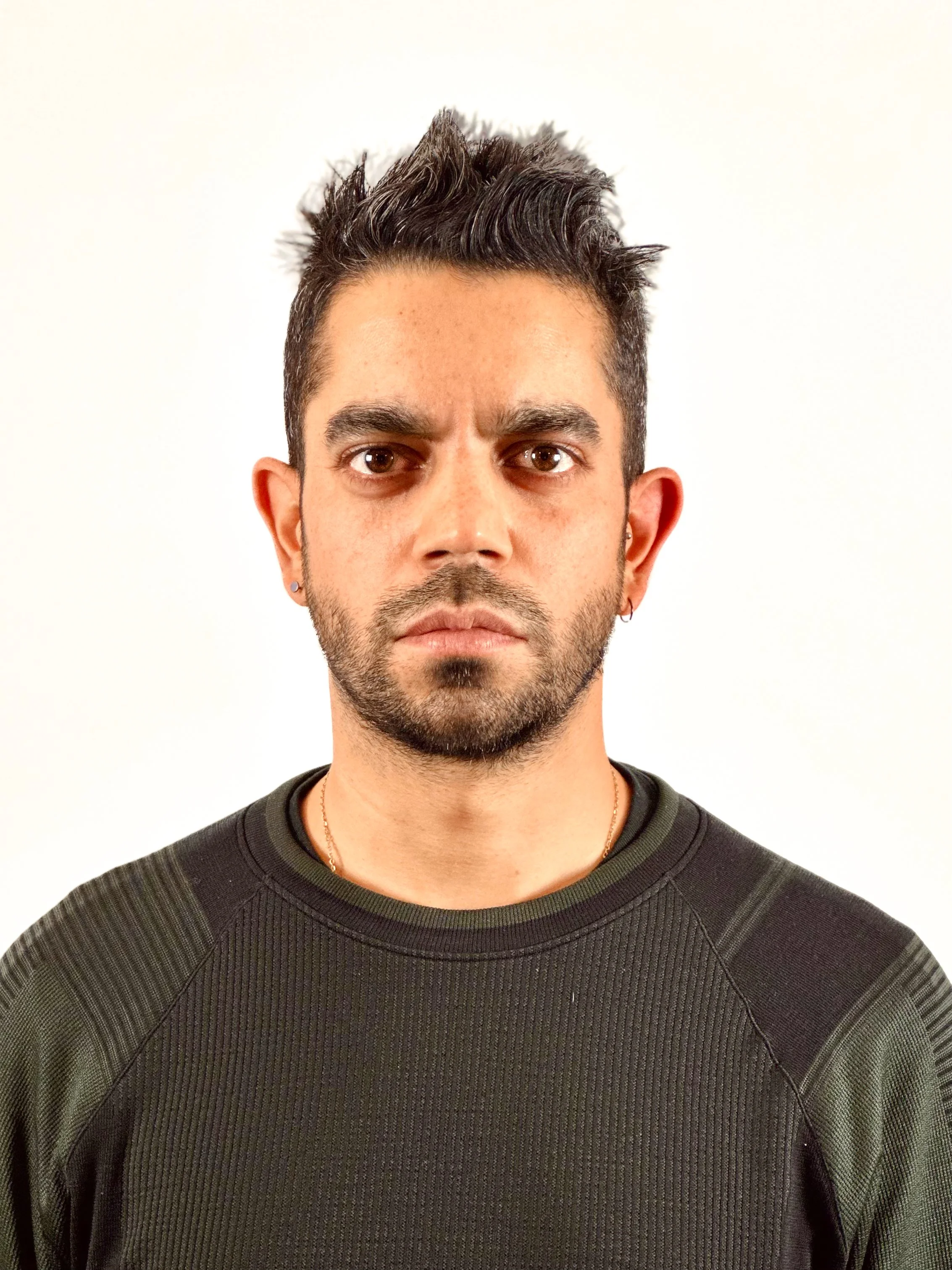Close-up of a man with dark hair styled upwards, tan skin, brown eyes, wearing a black athletic shirt, and standing against a plain white background.