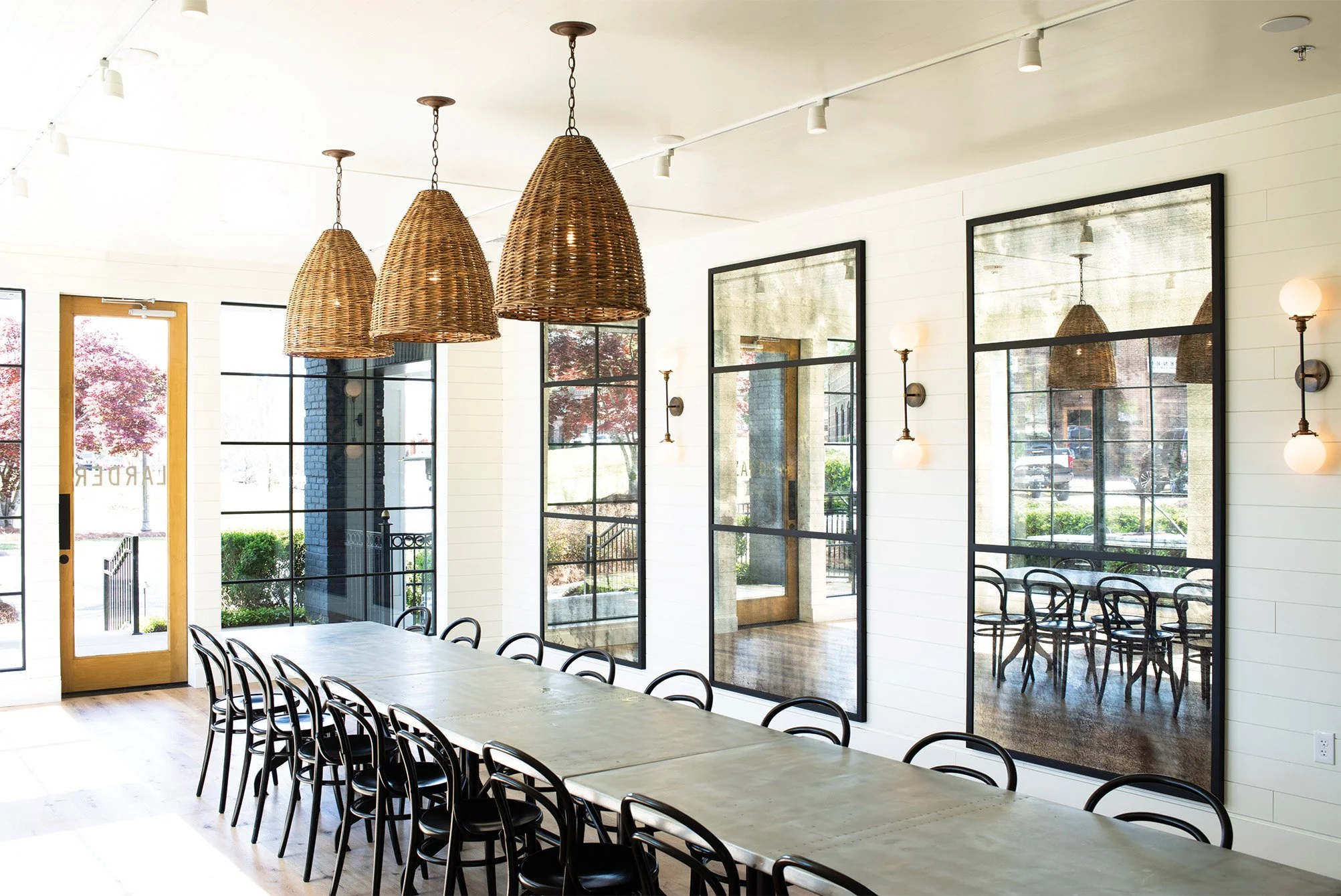 Bright dining or conference room with large windows, black chairs around a long table, and hanging woven wicker light fixtures.