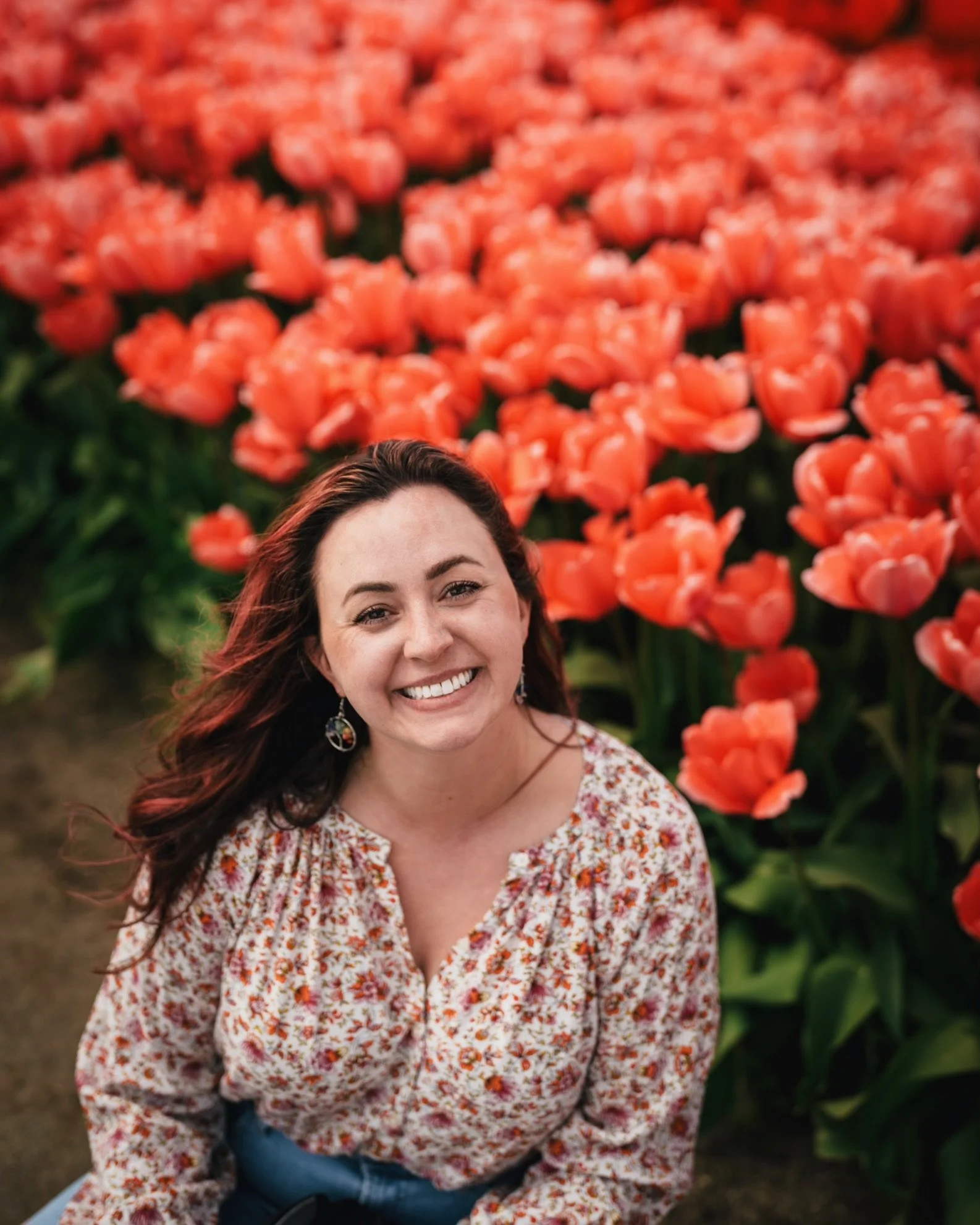Brooke smiling sitting in front of a field of tulips at the Skagit Tulip Festival