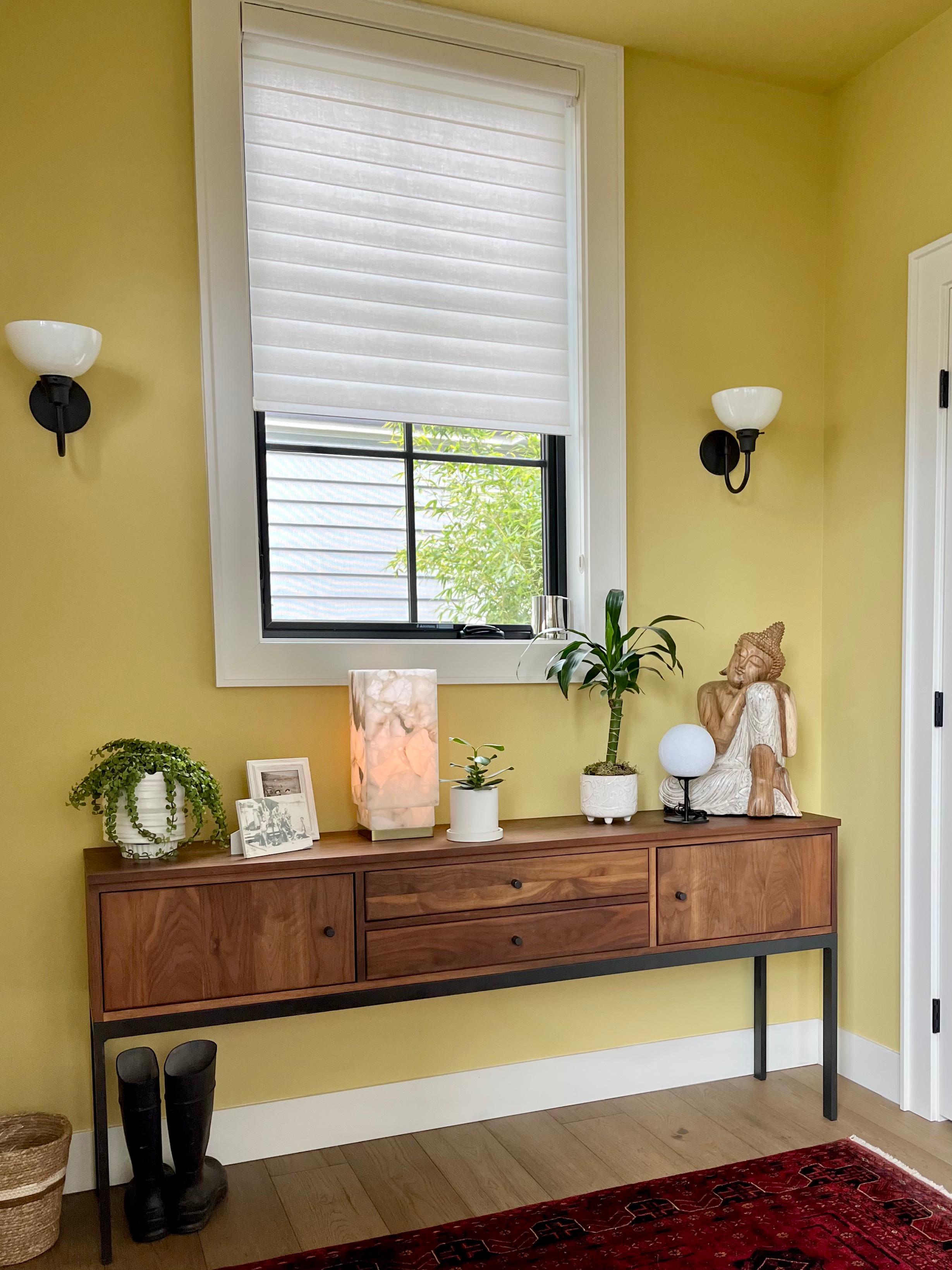Angled view of a warm walnut wood console, adorned with various plants and decor. The walls and ceiling are color-drenched in the color Mother Earth, an energizing and spunky chartreuse.