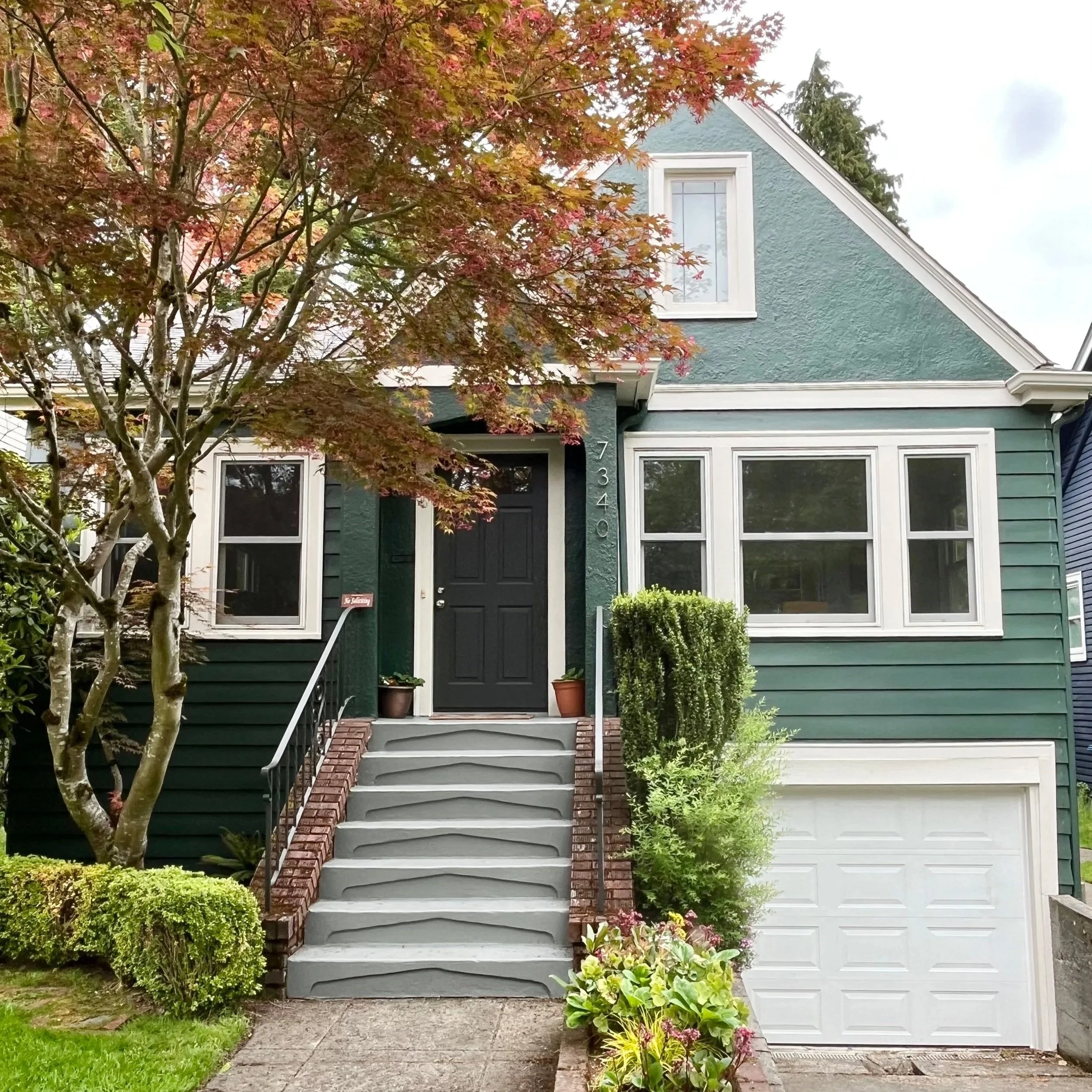 A two-story green tudor home with off-white trim with a warm charcoal front door.