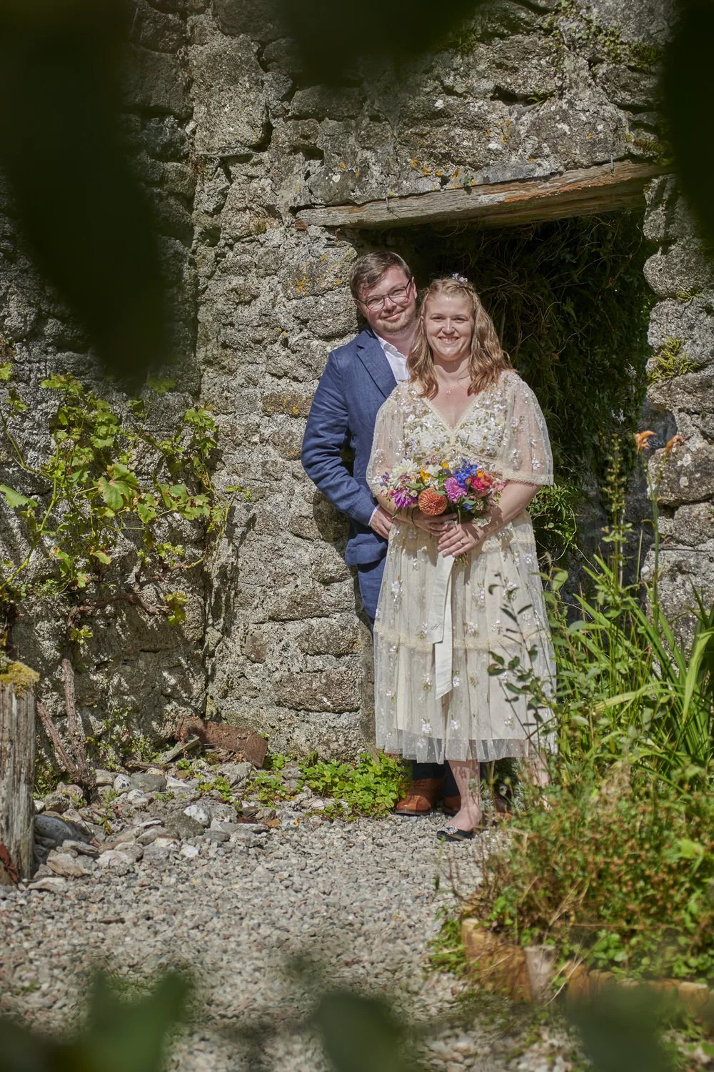 Bride and groom stand in the doorway of a stone courtyard in the sun.