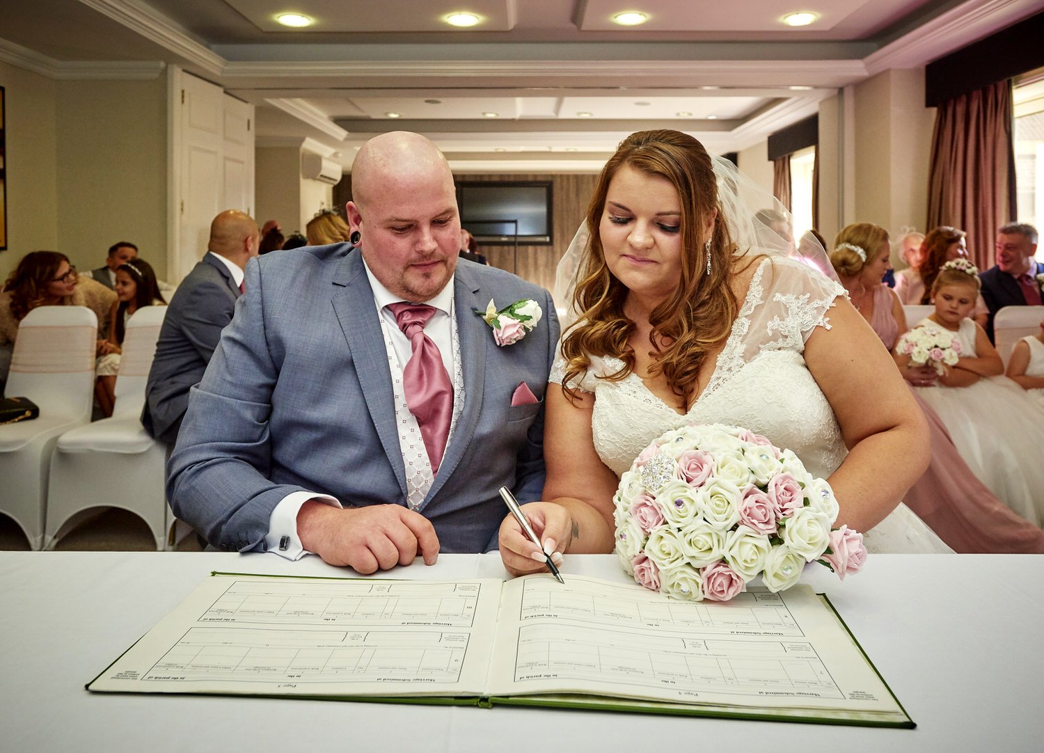 The bride and groom sign the register with their guests sat behind them.