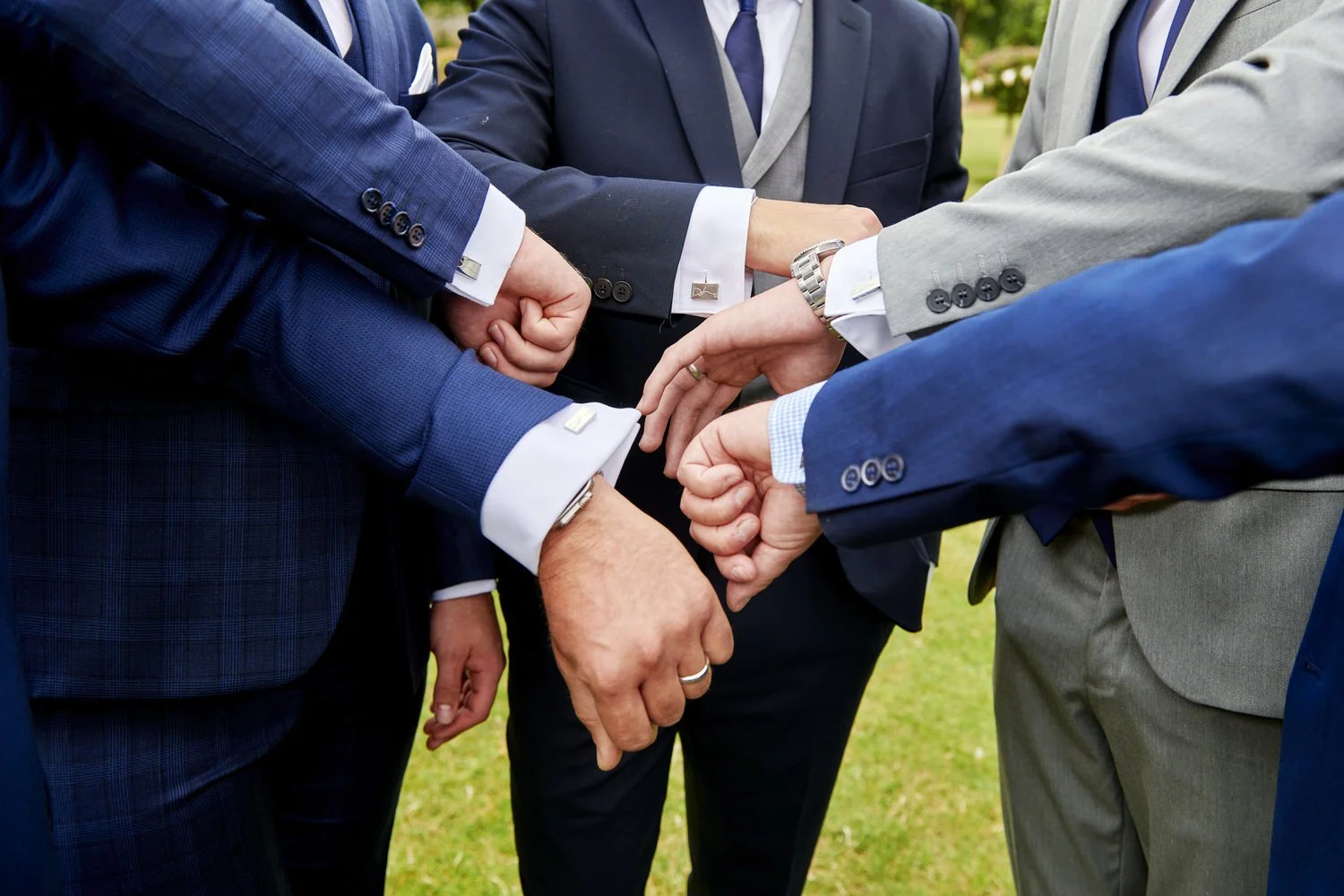 Close-up image of groom and groomsmen holding their cuffs together to show matching cufflinks.
