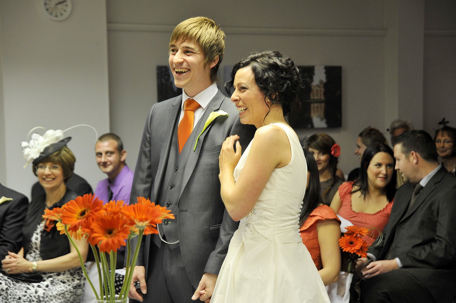 Bride and groom smile as they stand surrounded by guests as the ceremony starts.