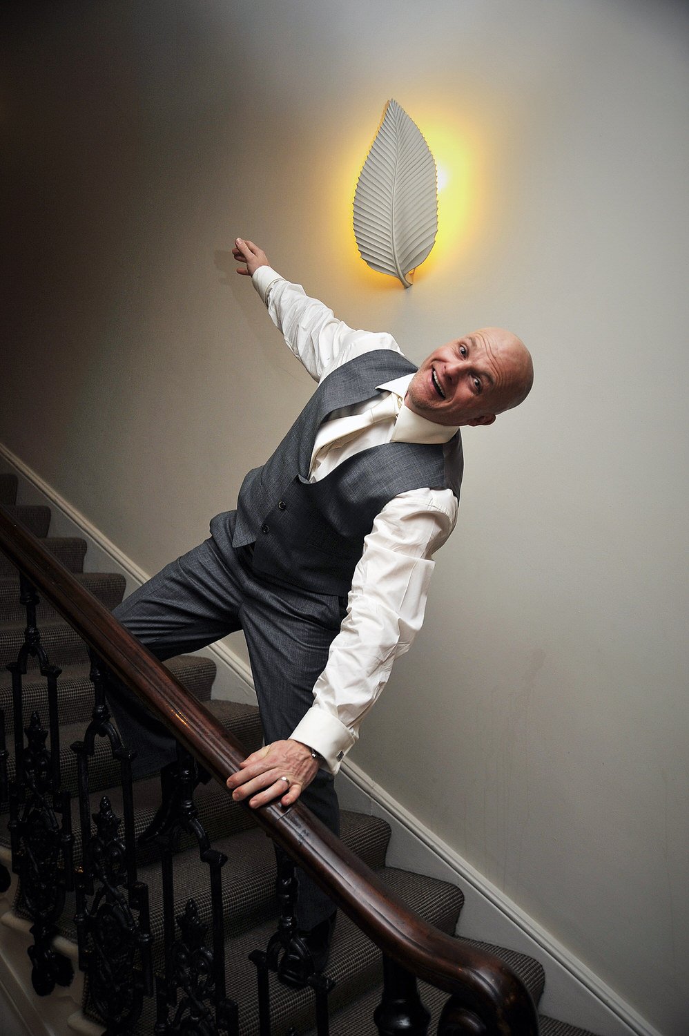 Groom leans on staircase banister and pulls a funny expression.