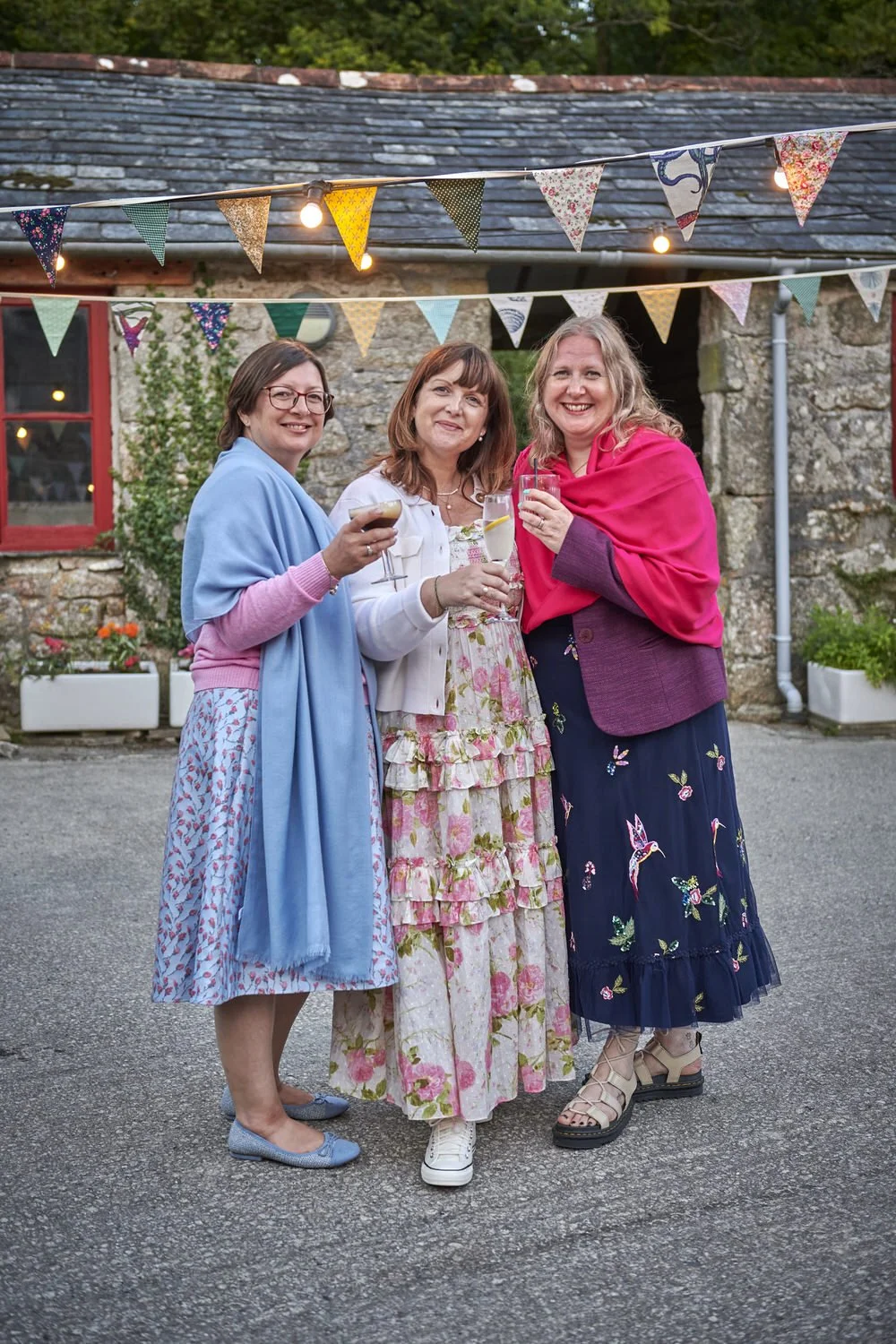 Three friends pose for picture together holding up drinks to the camera.