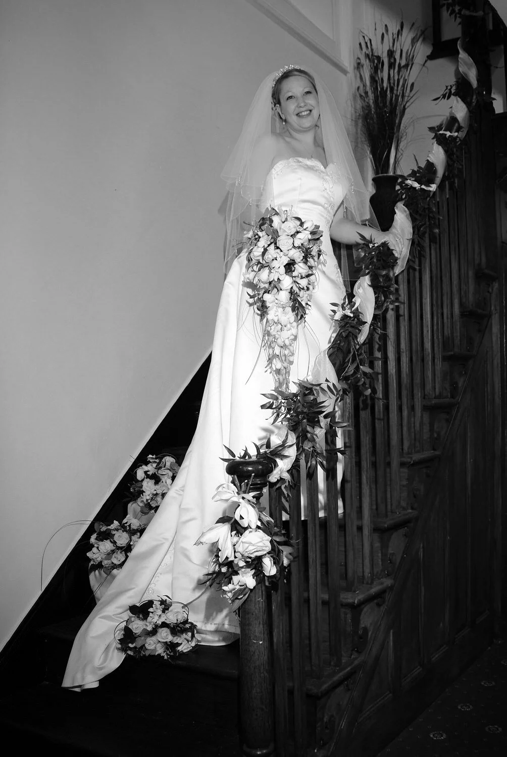 Bride poses on a steep staircase, holding the banister and looking at the camera.